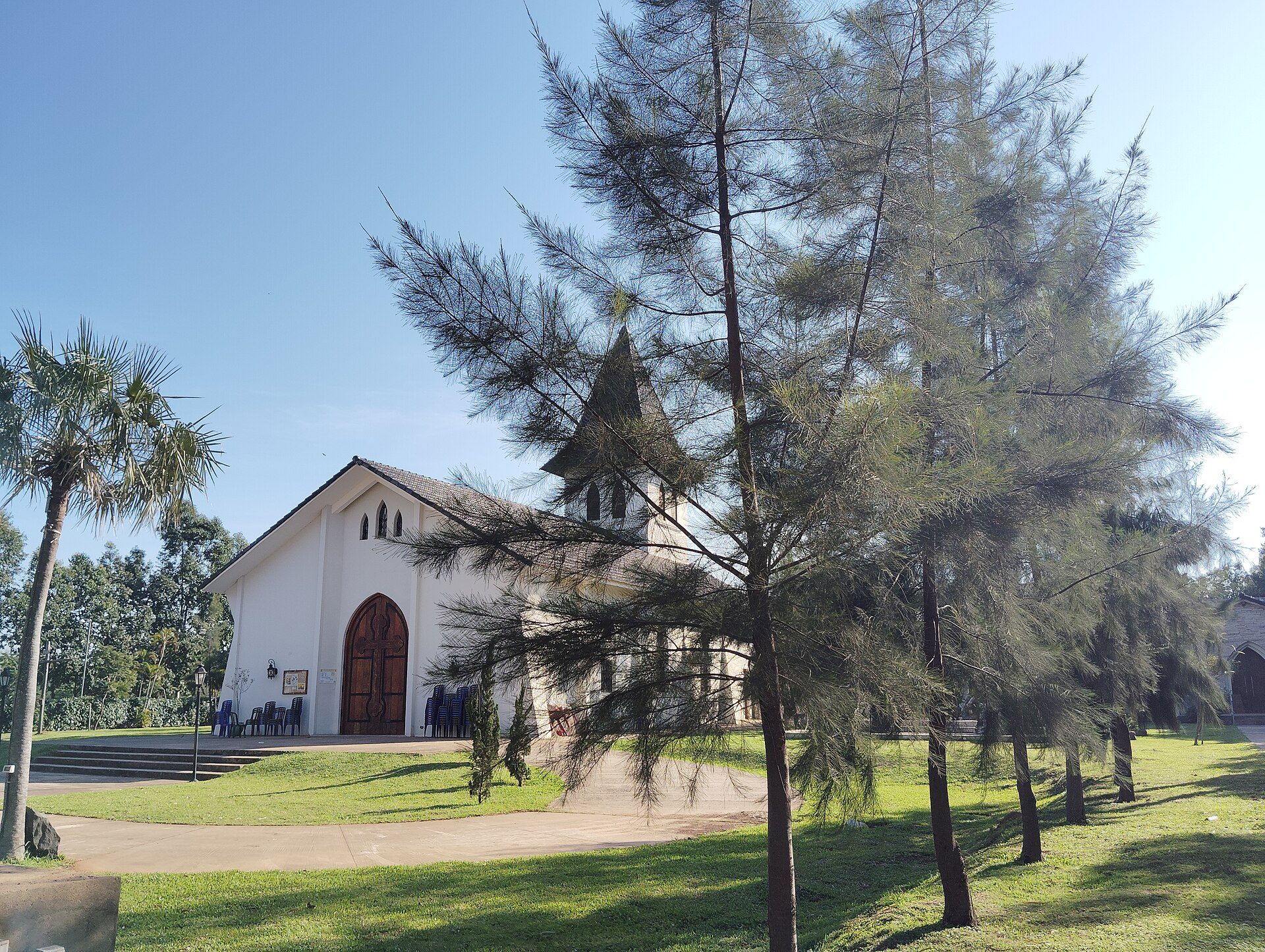 A white church with a tall steeple, surrounded by green trees and a clear blue sky.