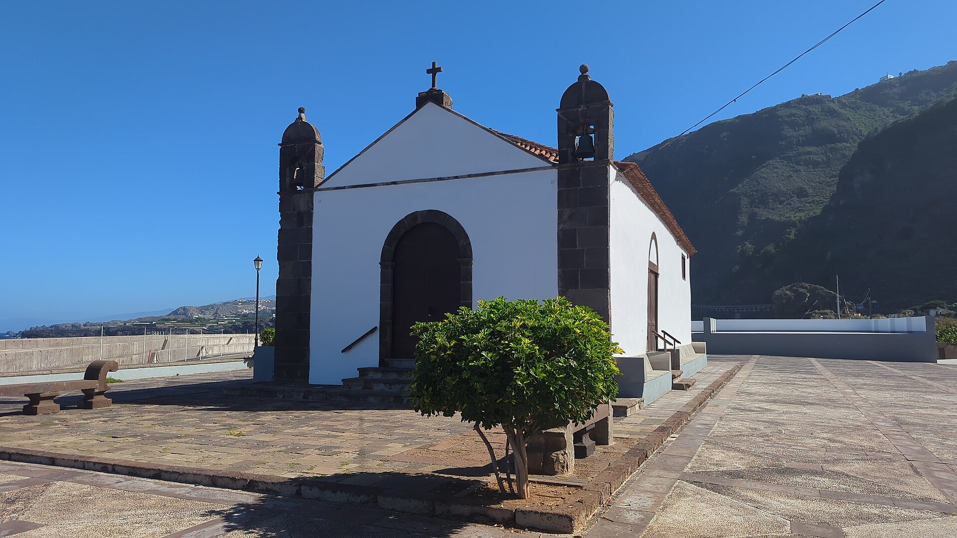 Small white church with twin bell towers, scenic mountain view, stone-paved courtyard.