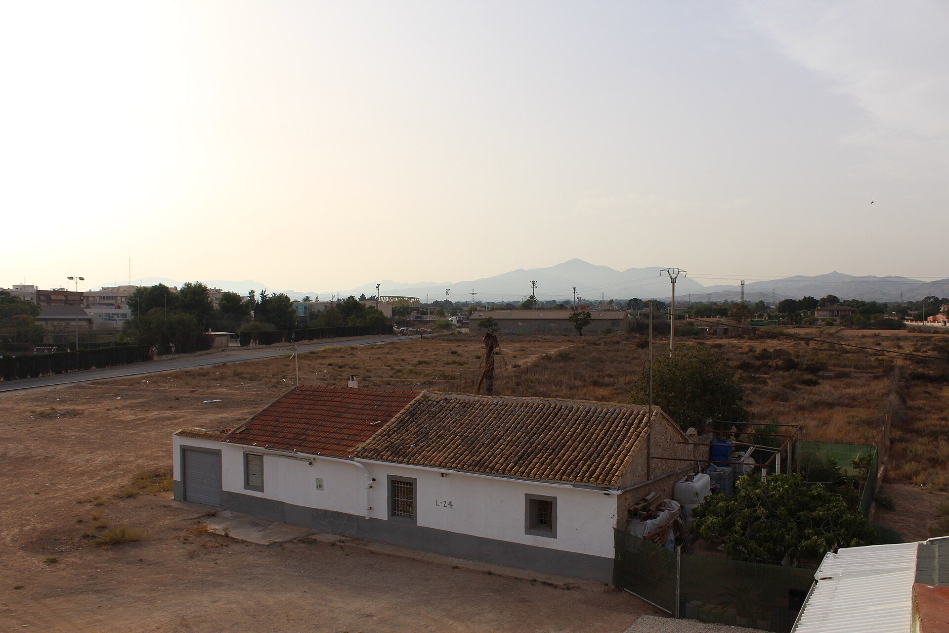 Small white house with red roof, surrounded by dry grass, distant mountains visible.