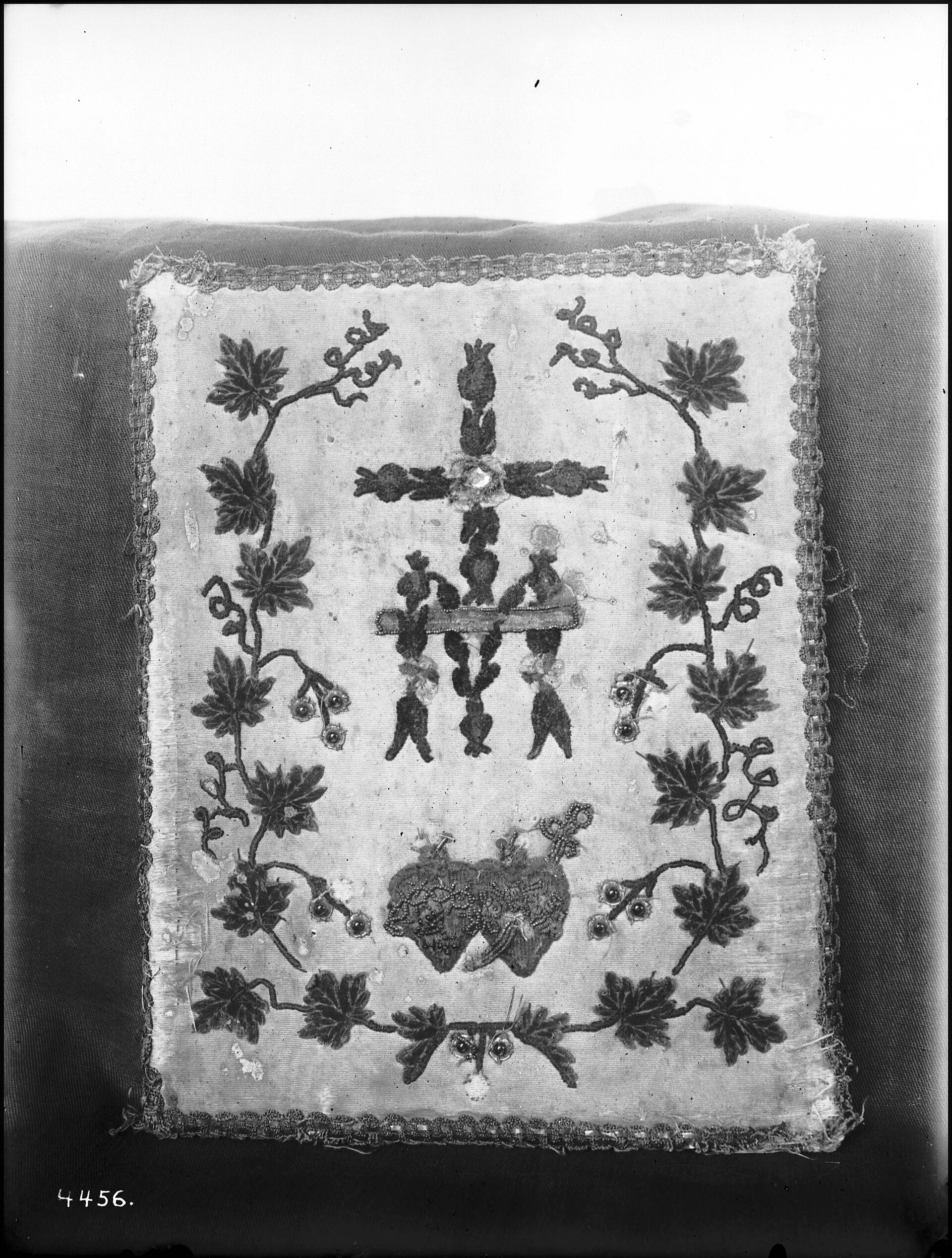 Black and white photo of a vintage tapestry with floral and heraldic designs.