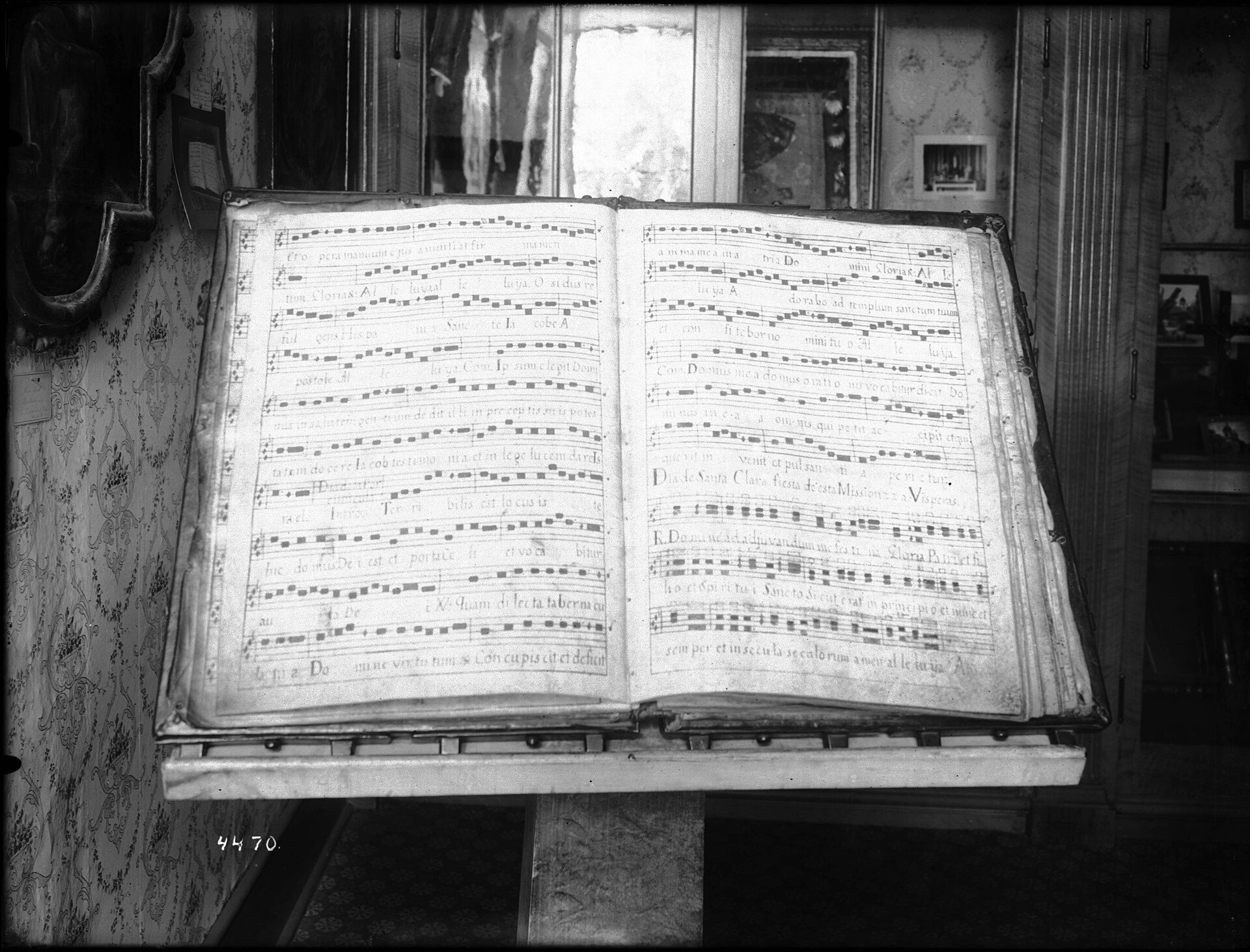 An open music book on a stand in a vintage room with framed pictures.