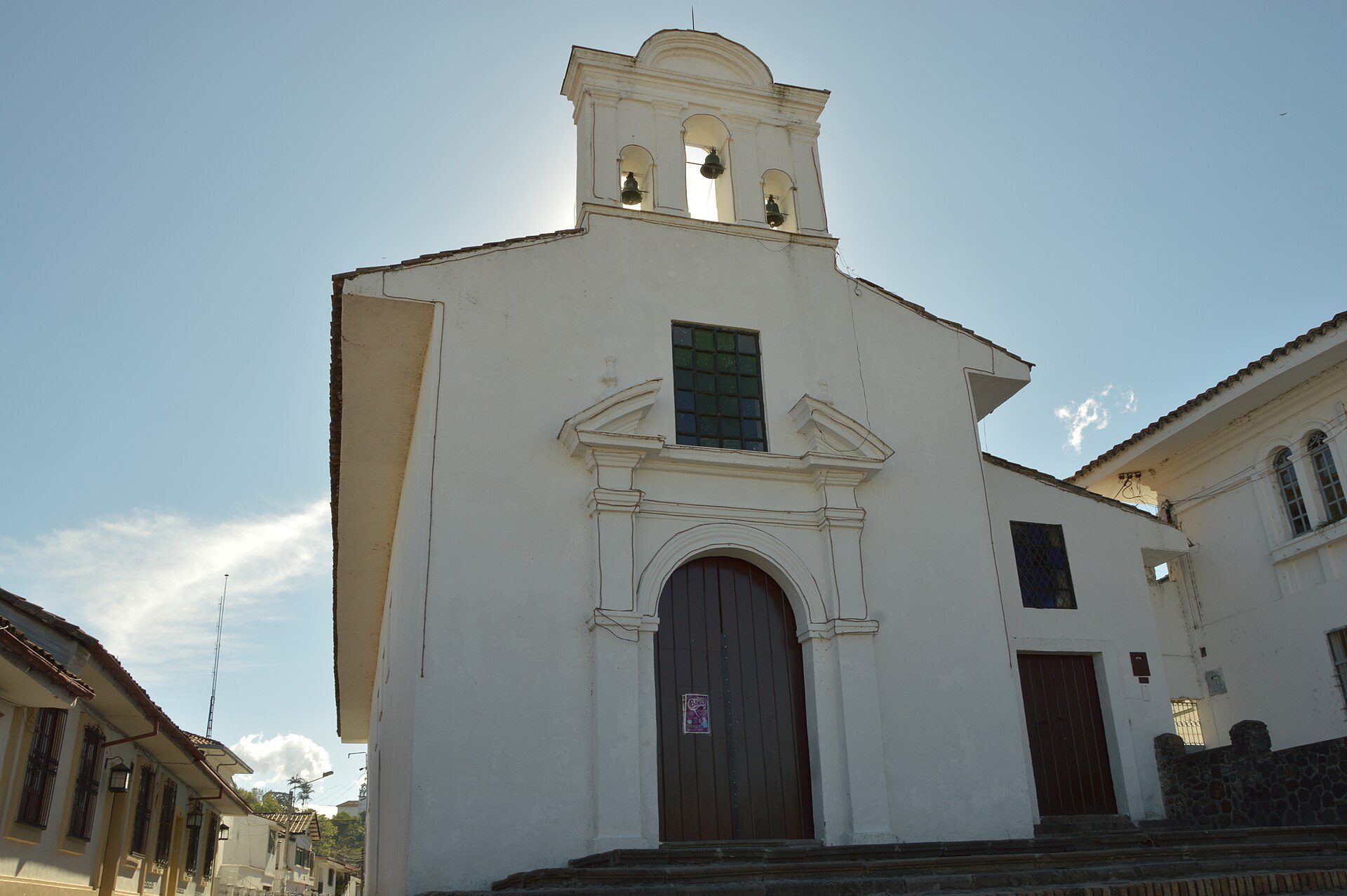 White church with bell tower, wooden doors, and clear blue sky.