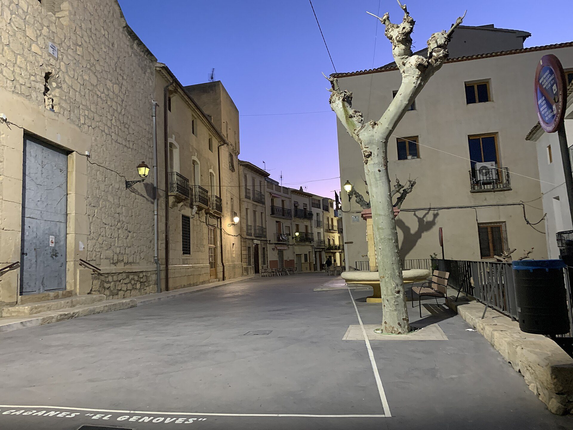 Alt text: Stone building with arched windows, quiet street, and a tree.