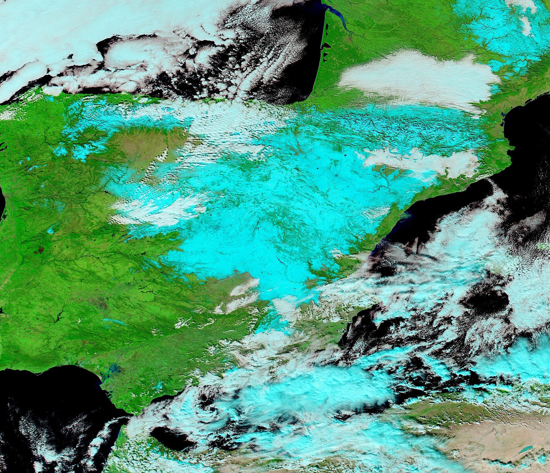 Alt text: Aerial view of a green landscape with scattered clouds and a blue sky.