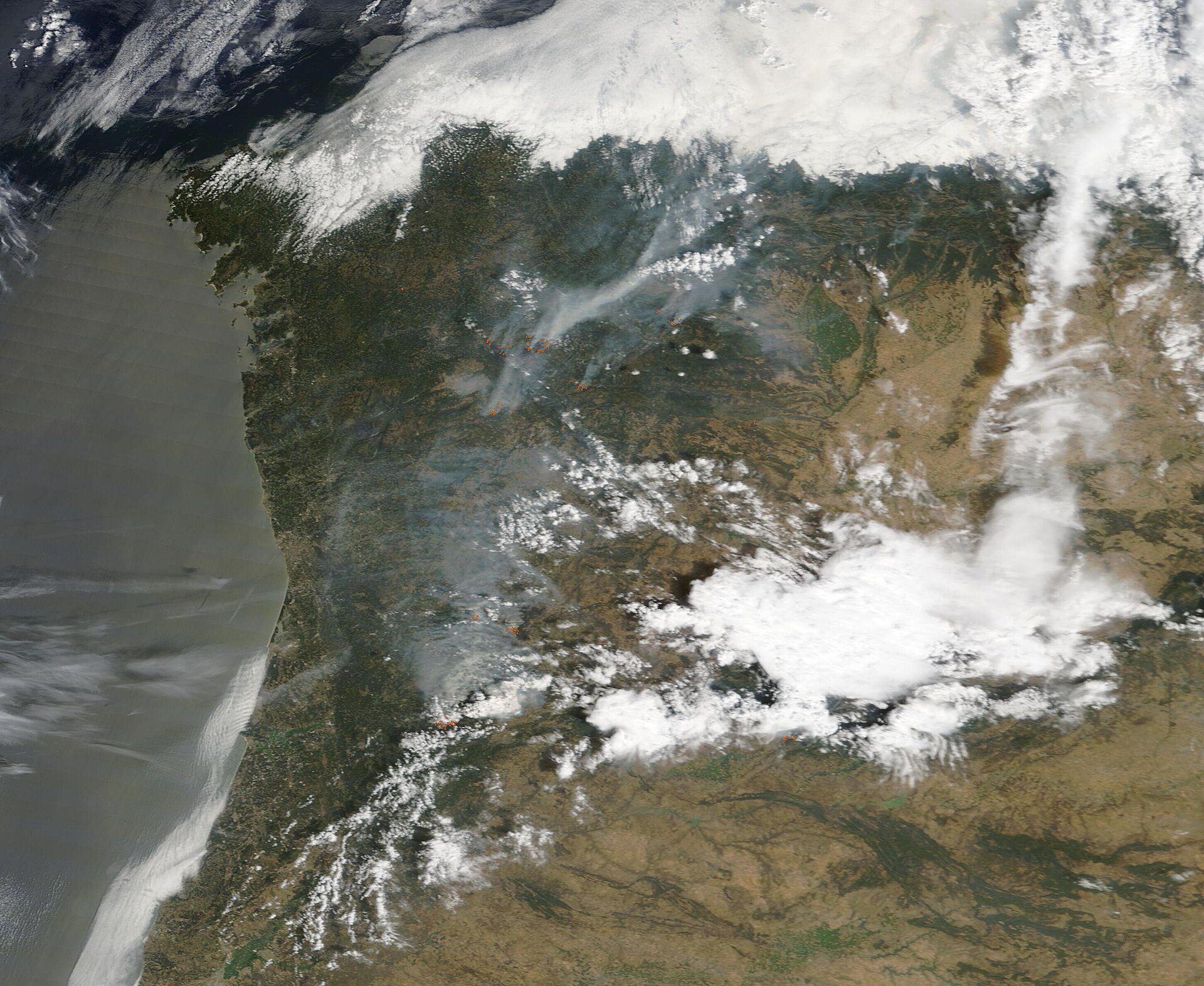 Aerial view of a coastal landscape with mountains, forests, and clouds.