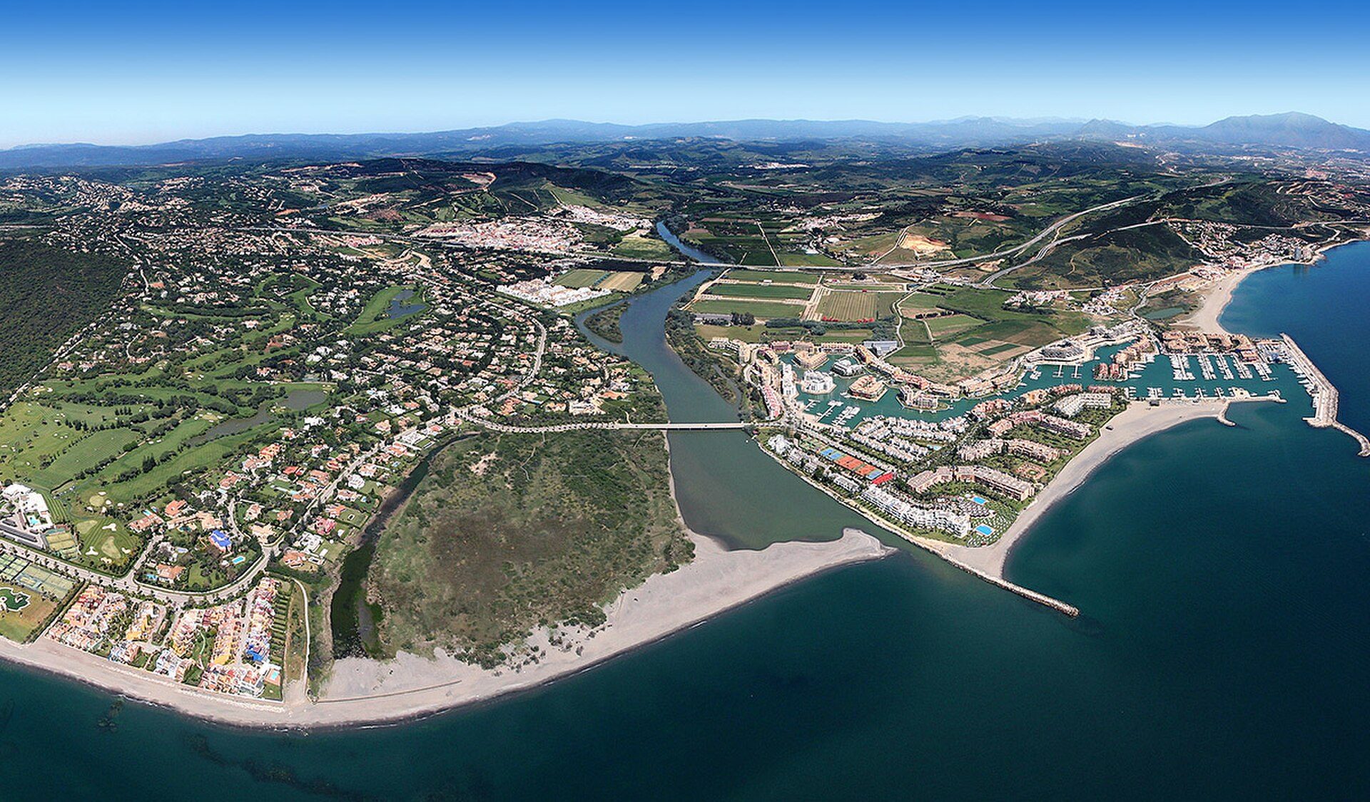 Aerial view of a coastal town with a river, beach, and greenery.