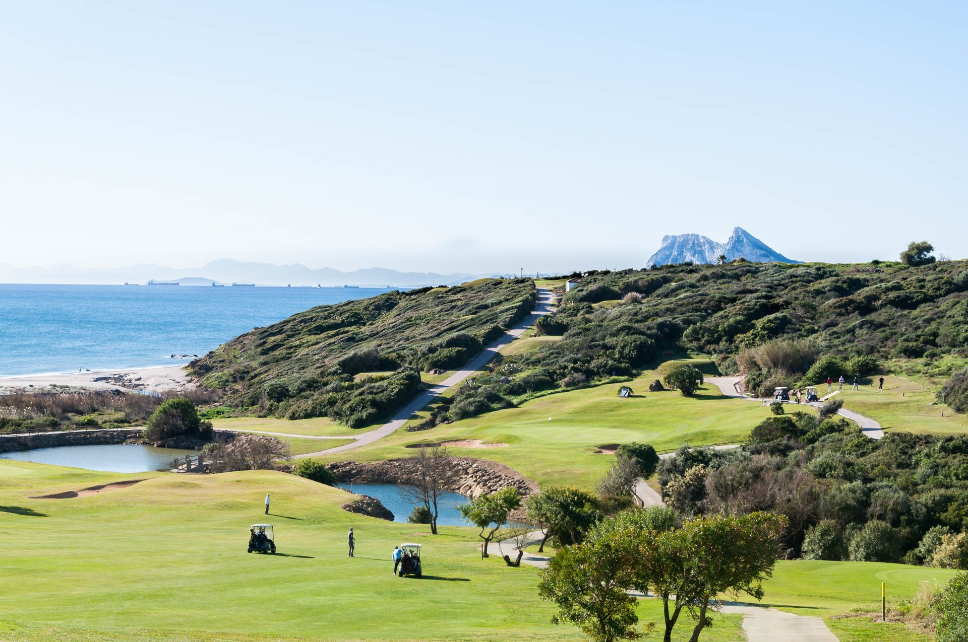 Luxury golf resort with ocean view, green fairways, and mountain backdrop.