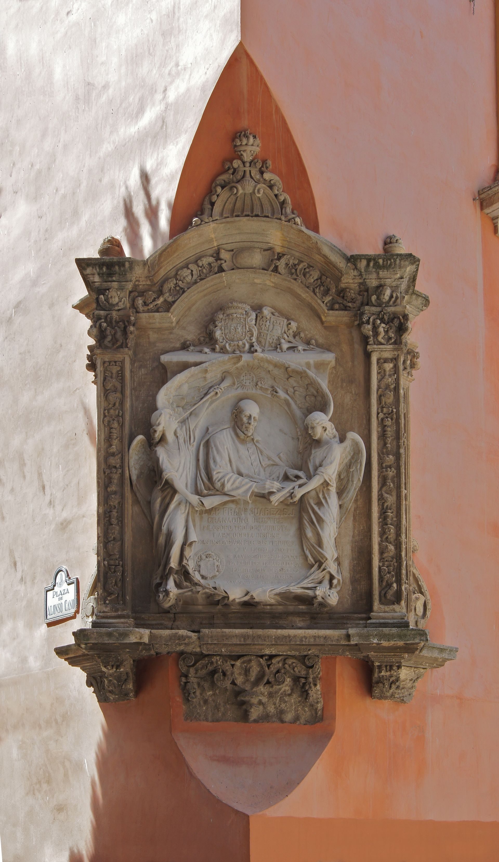 Alt text: Ornate stone relief with angelic figures and Latin inscription on a peach-colored wall.