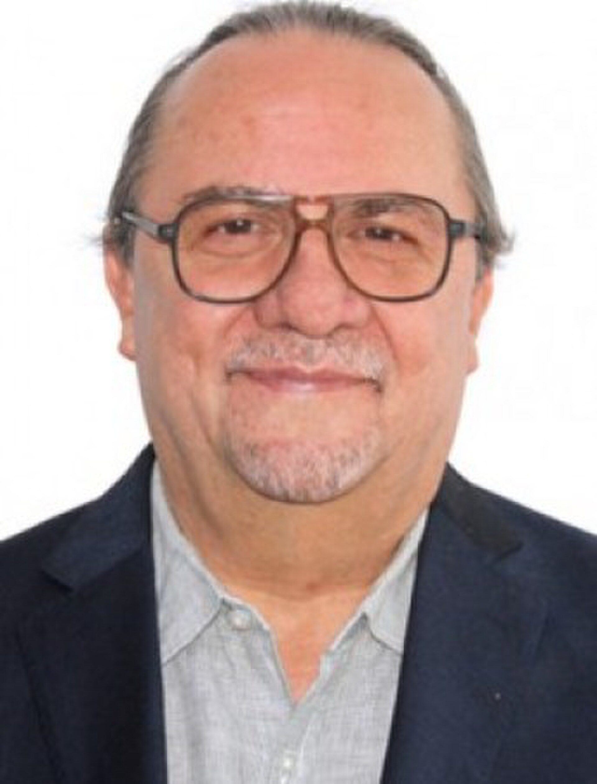 A man in a suit and glasses smiles for a professional headshot.