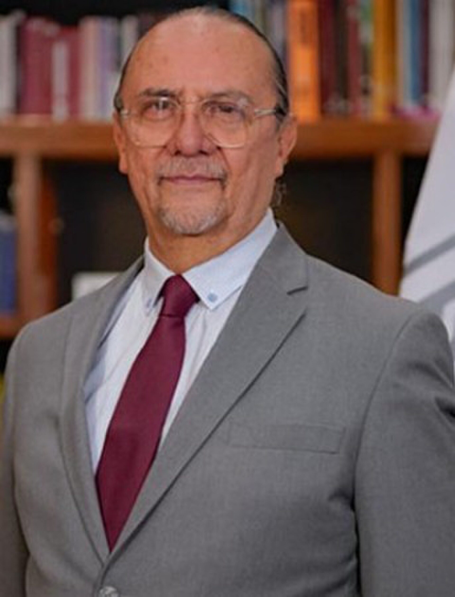 A man in a suit and tie stands in a room with bookshelves.