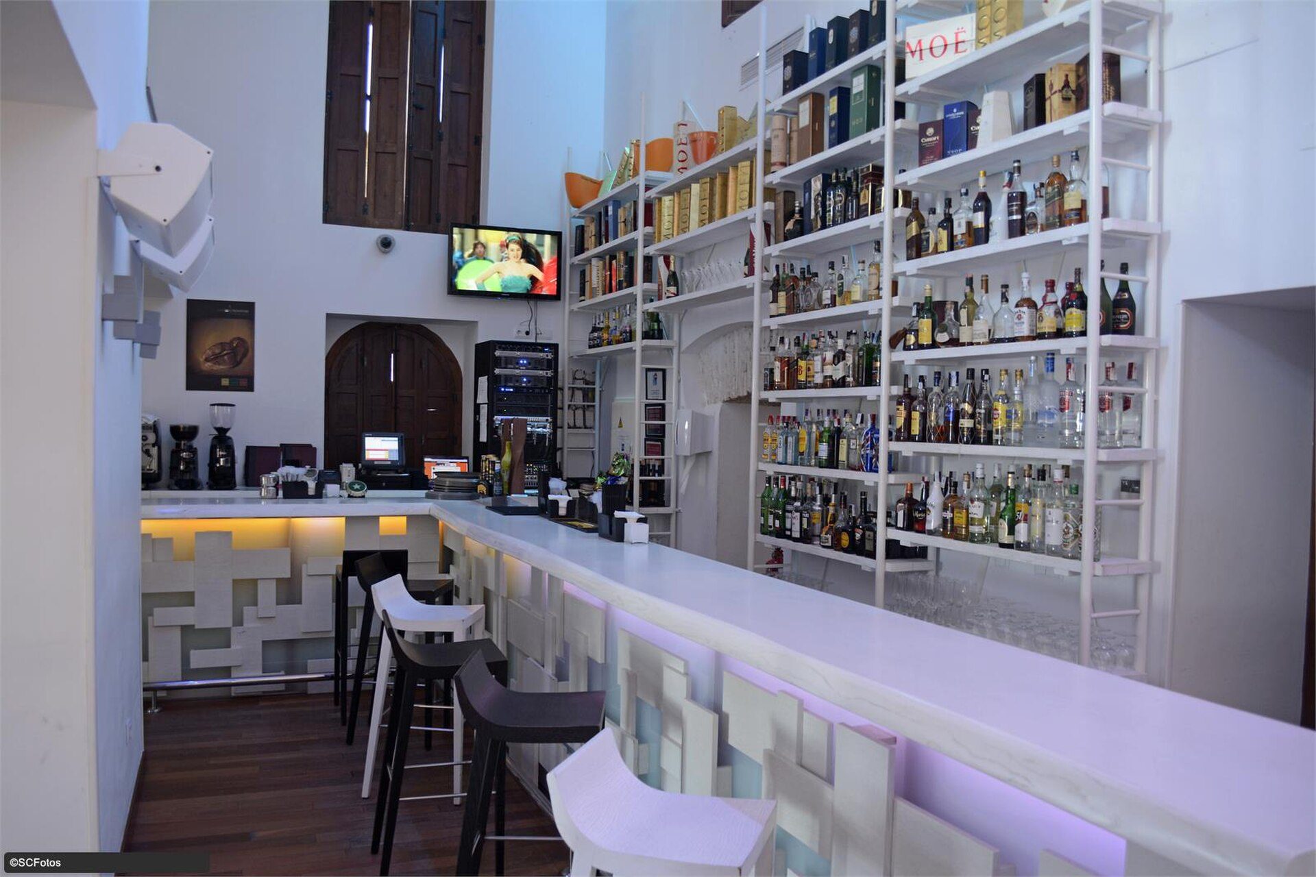 Modern bar with white shelves, flat-screen TV, and a cozy seating area.