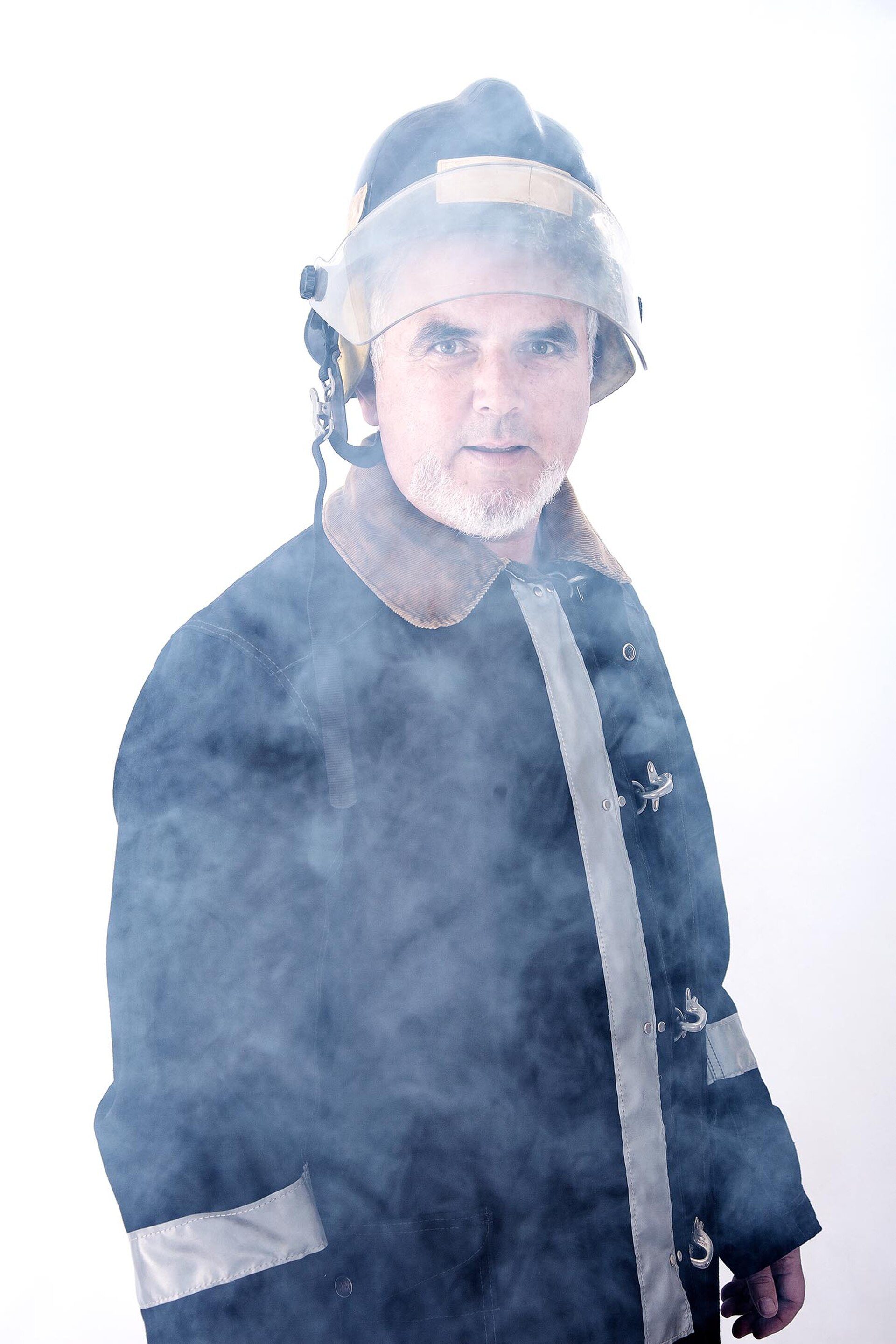 A firefighter in full gear stands amidst smoke, wearing a helmet and jacket.