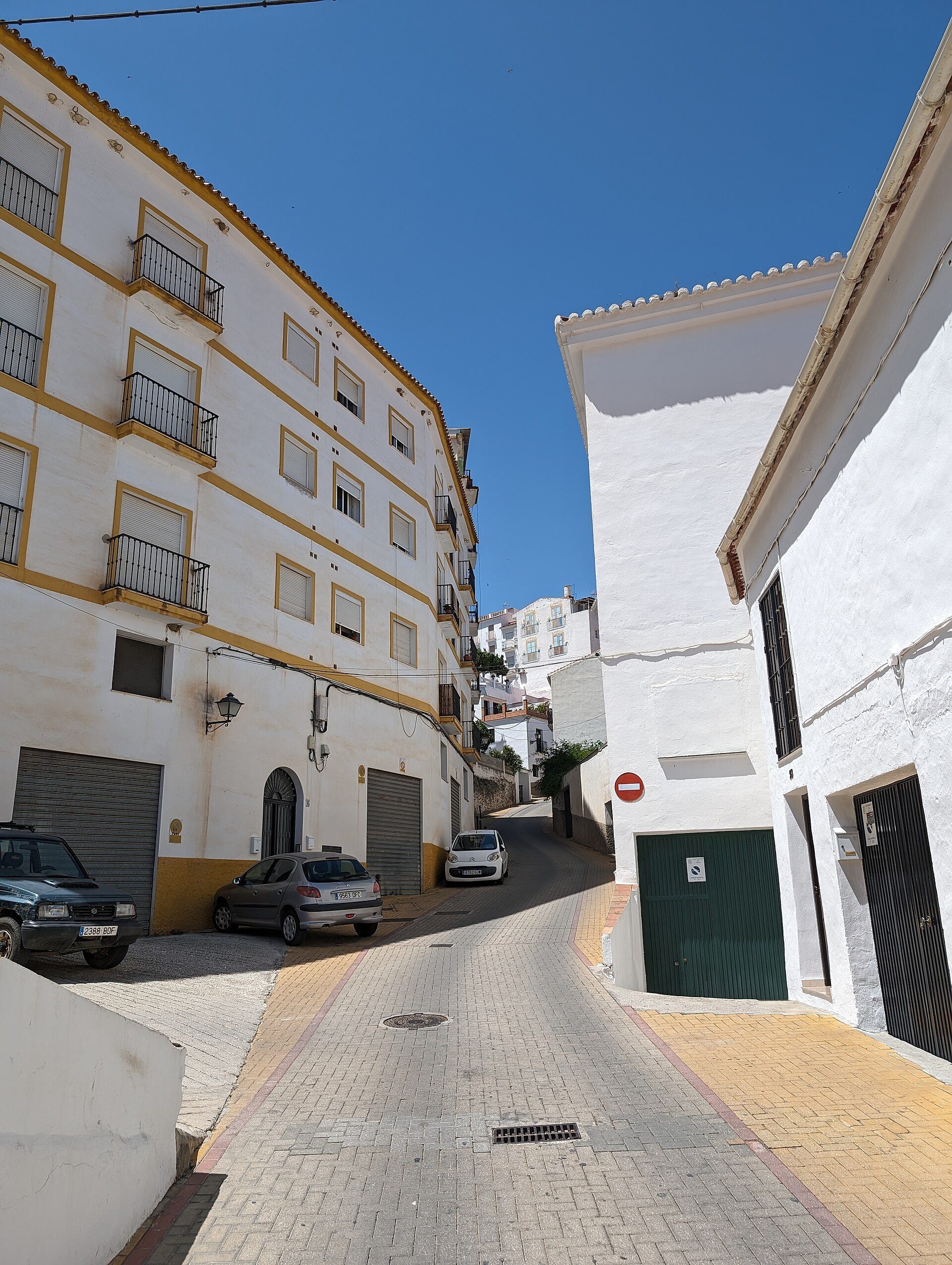Alt text: White building with yellow trim, balcony, and garage, sunny street view.