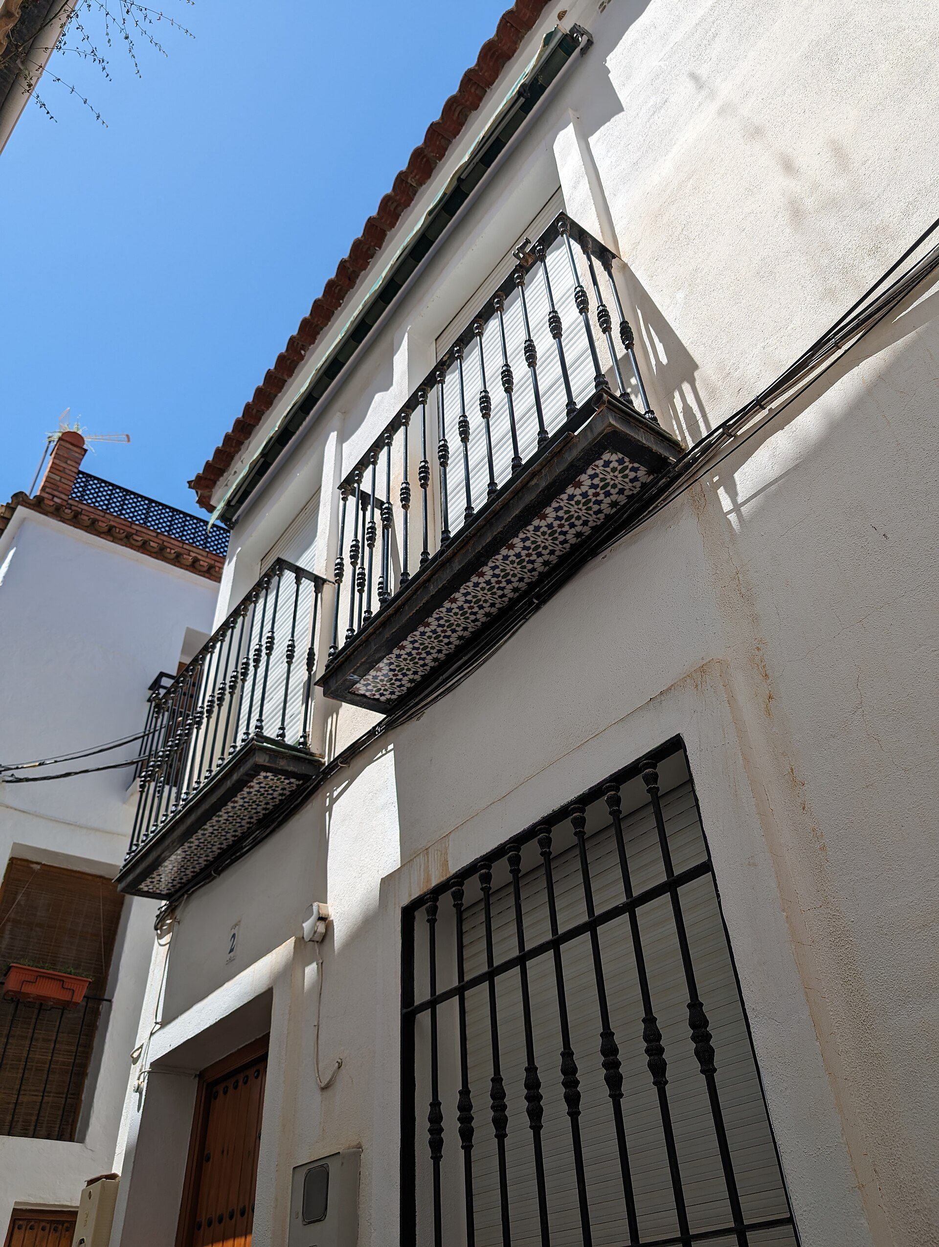 Balcony with metal railing, white building, clear blue sky, street view.