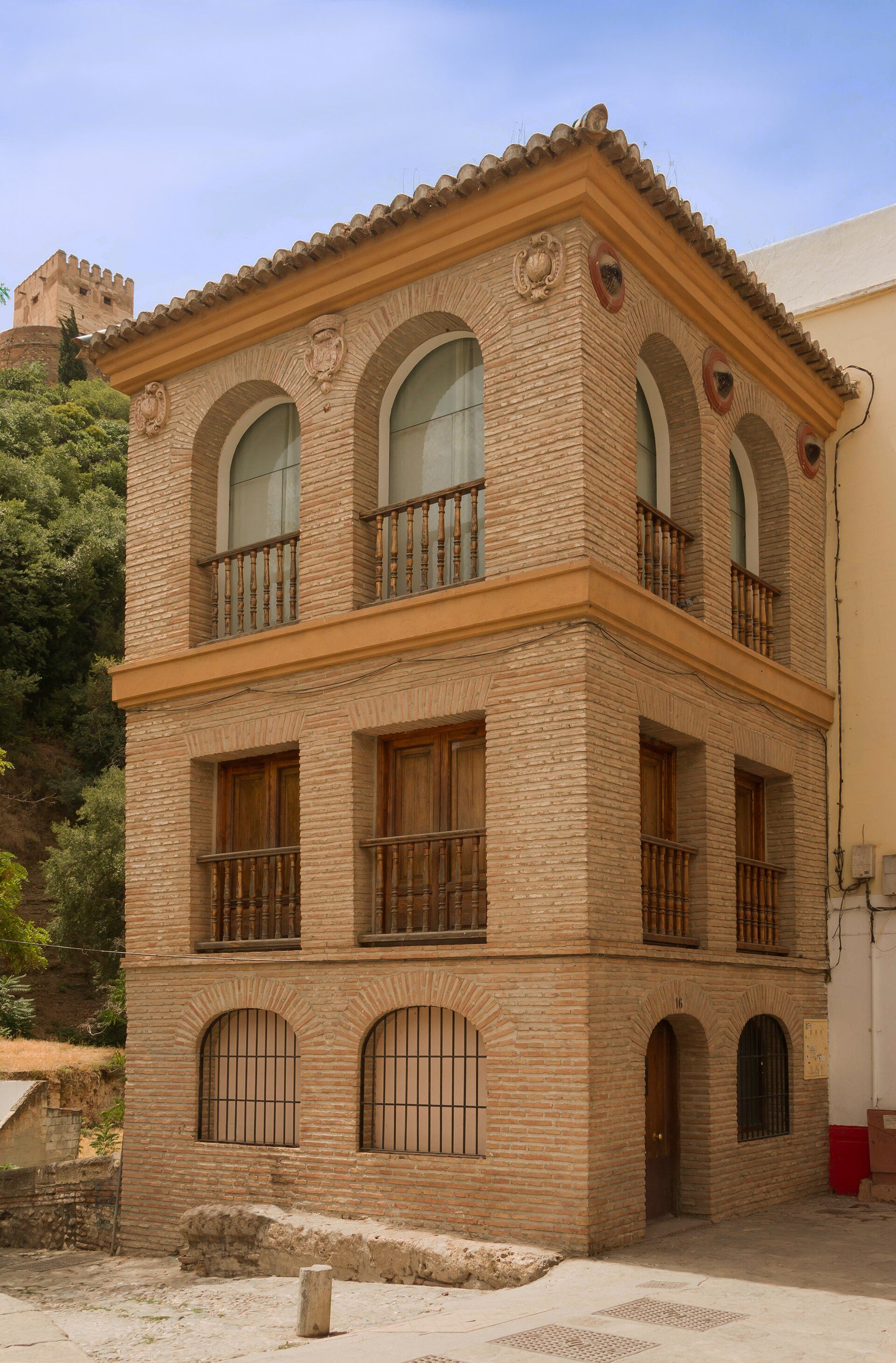 Traditional brick building with arched windows, balcony, and mountain view.