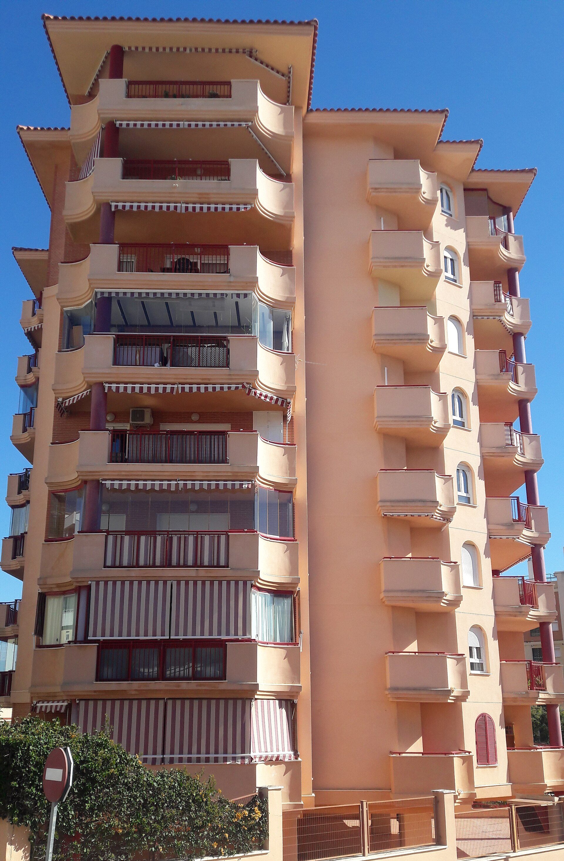 A modern apartment building with balconies, large windows, and a sunny view.