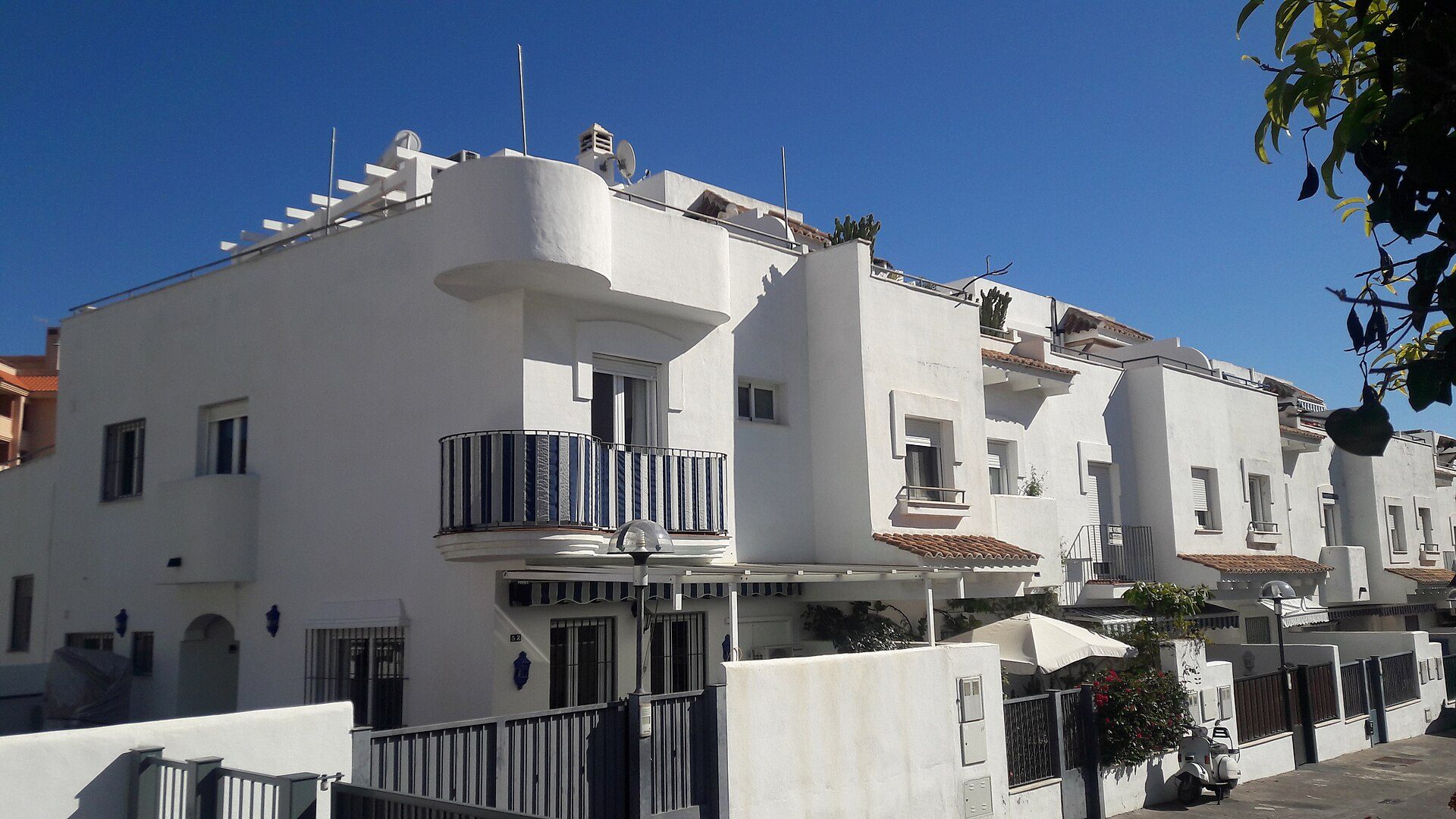 White Mediterranean-style villa with balconies, terracotta roof, and clear blue sky view.