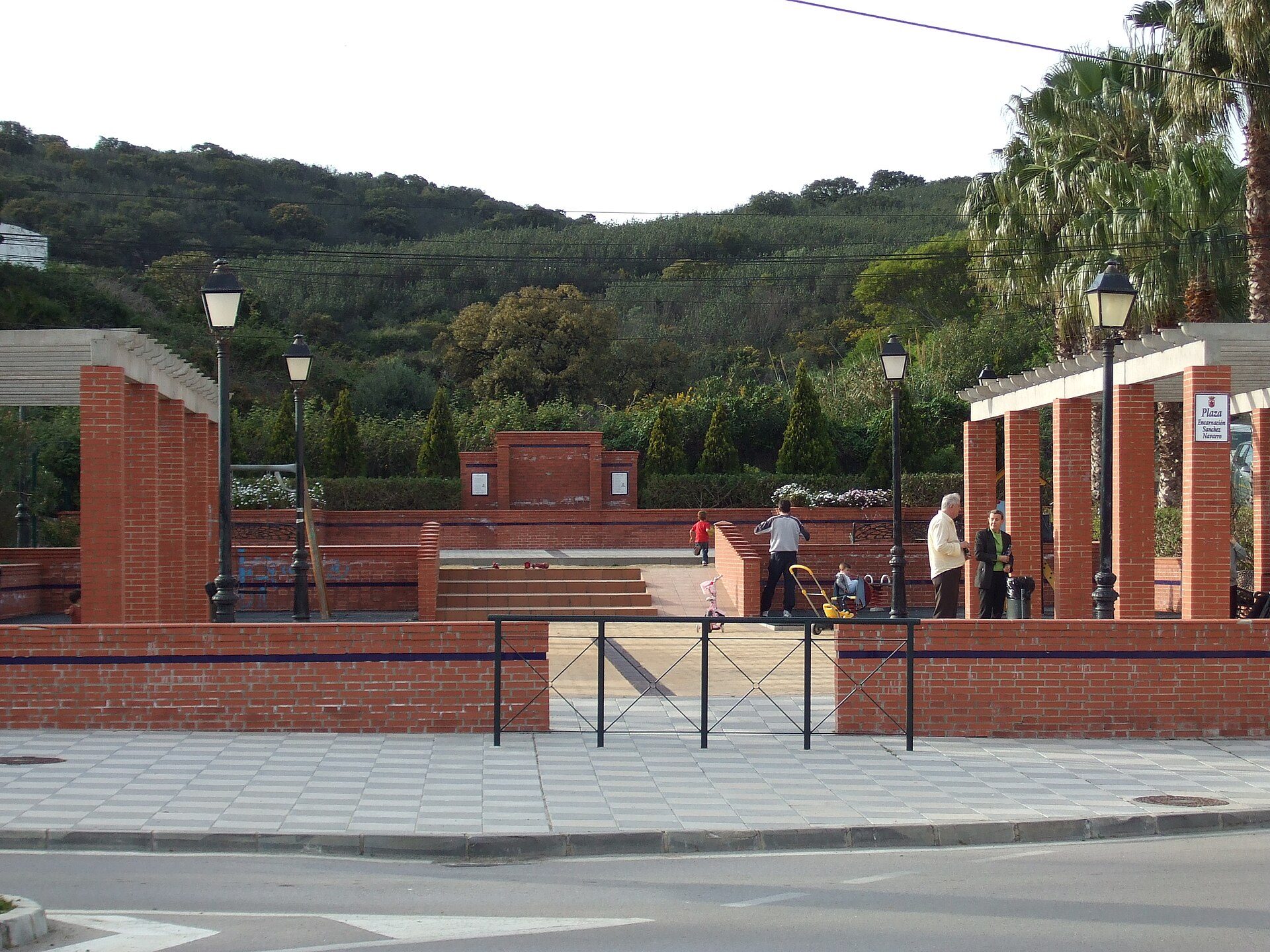 Alt text: Outdoor terrace with brick walls, palm trees, and a view of a hilly landscape.