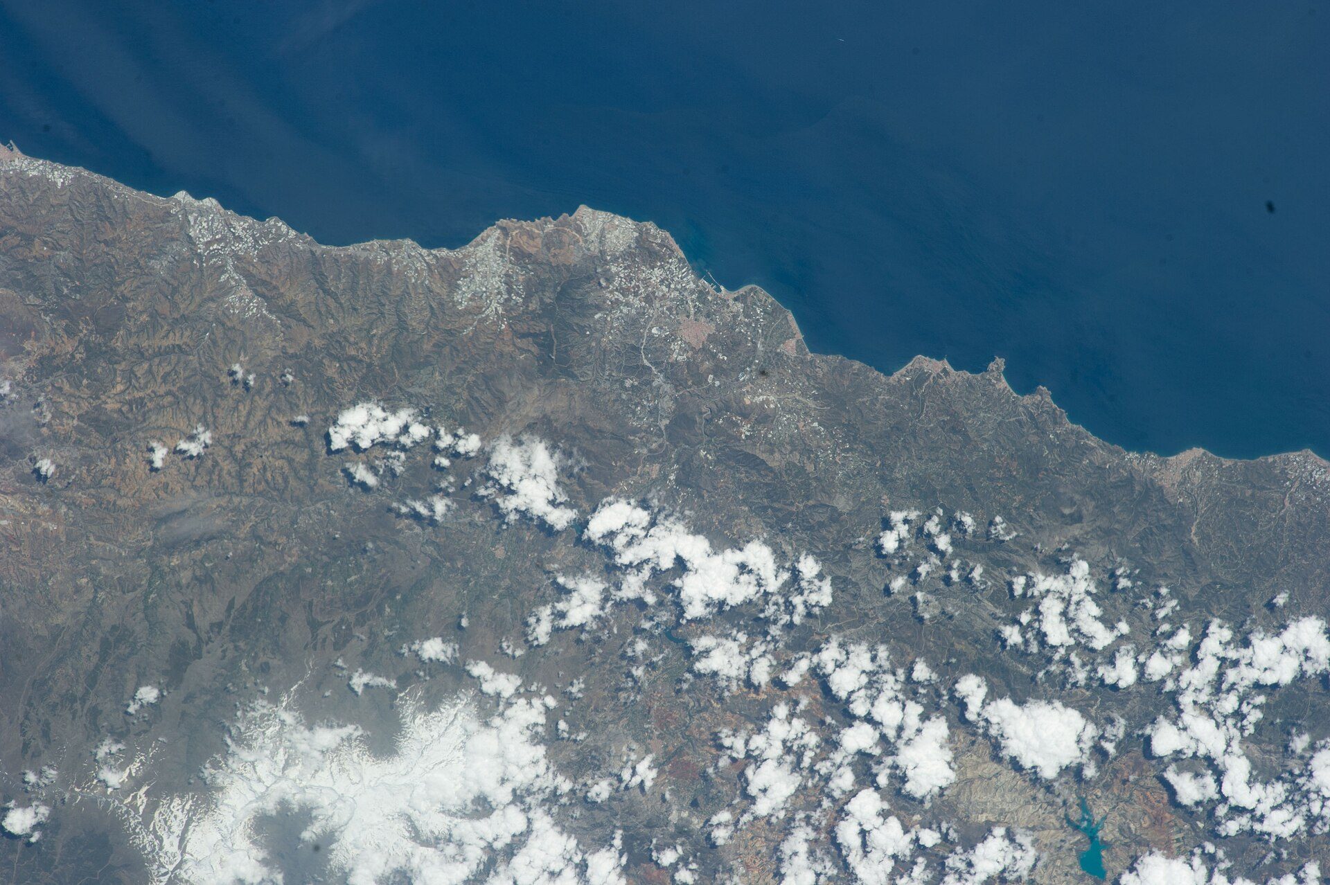 Aerial view of a coastal landscape with mountains, clouds, and the ocean.