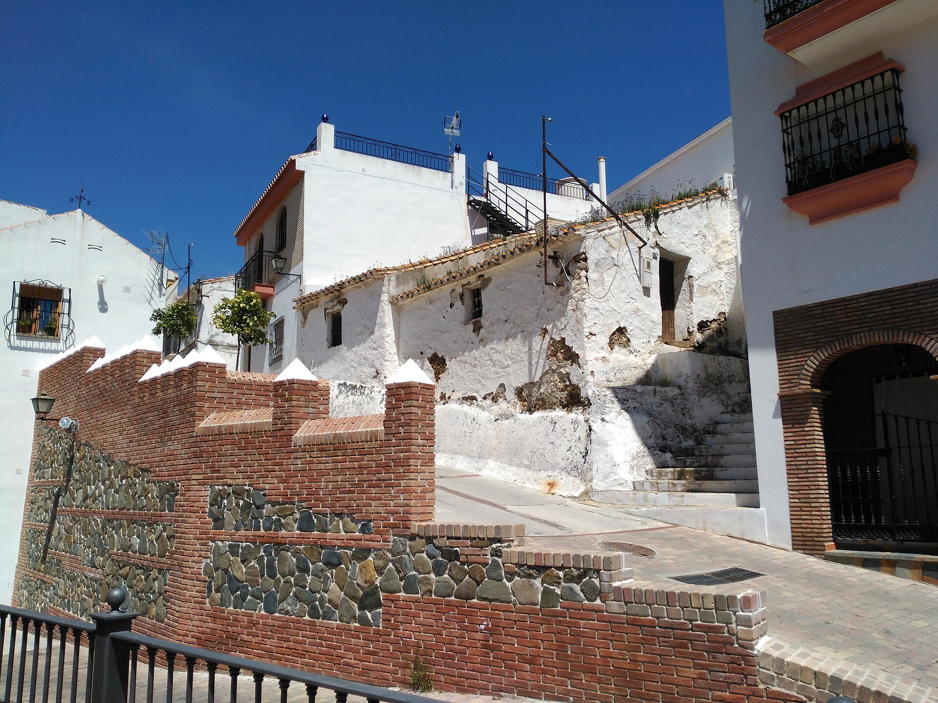 Traditional white-washed house with a balcony, brick steps, and a clear blue sky view.