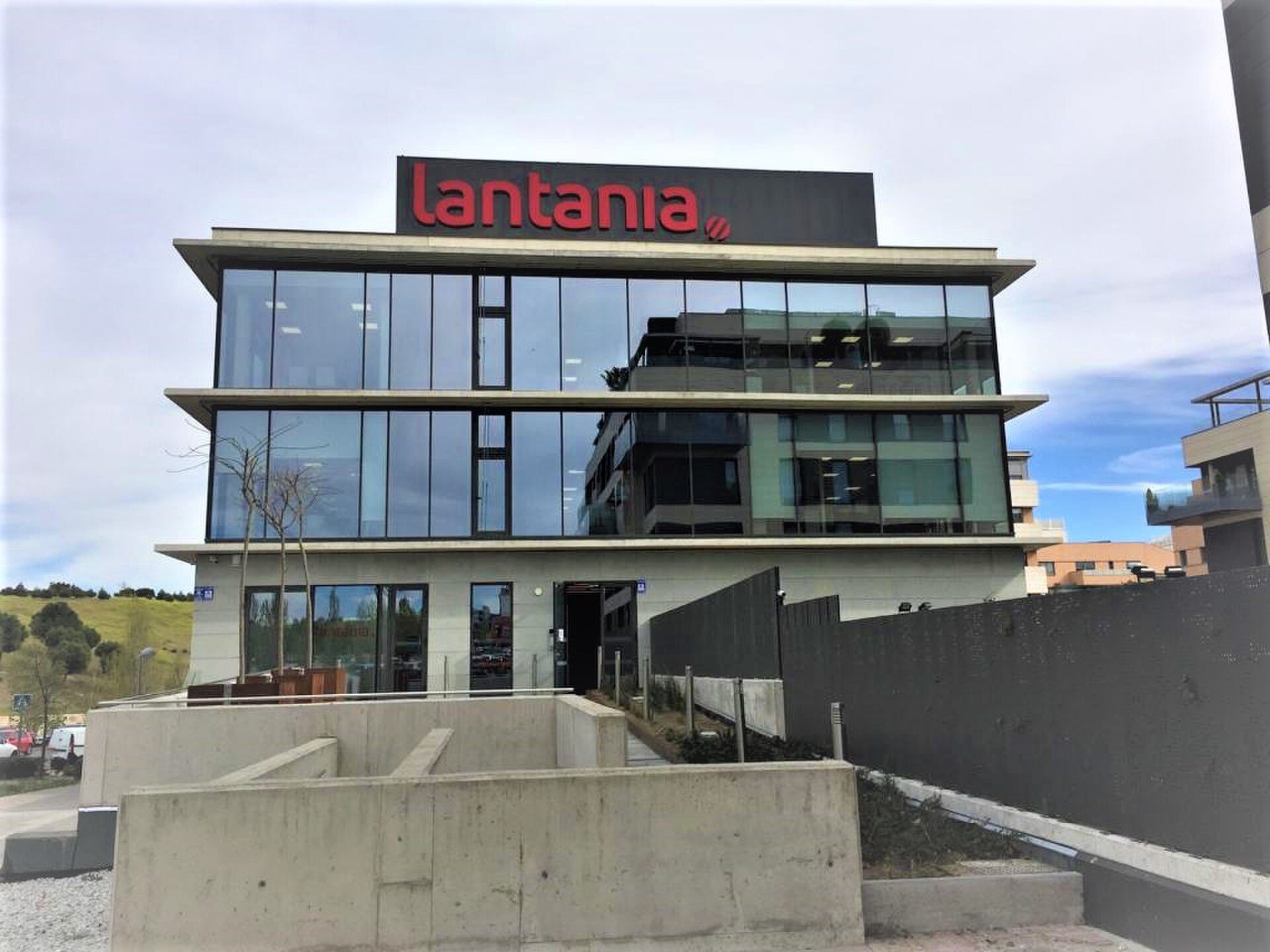 Modern office building with glass facade, rooftop garden, and parking area.