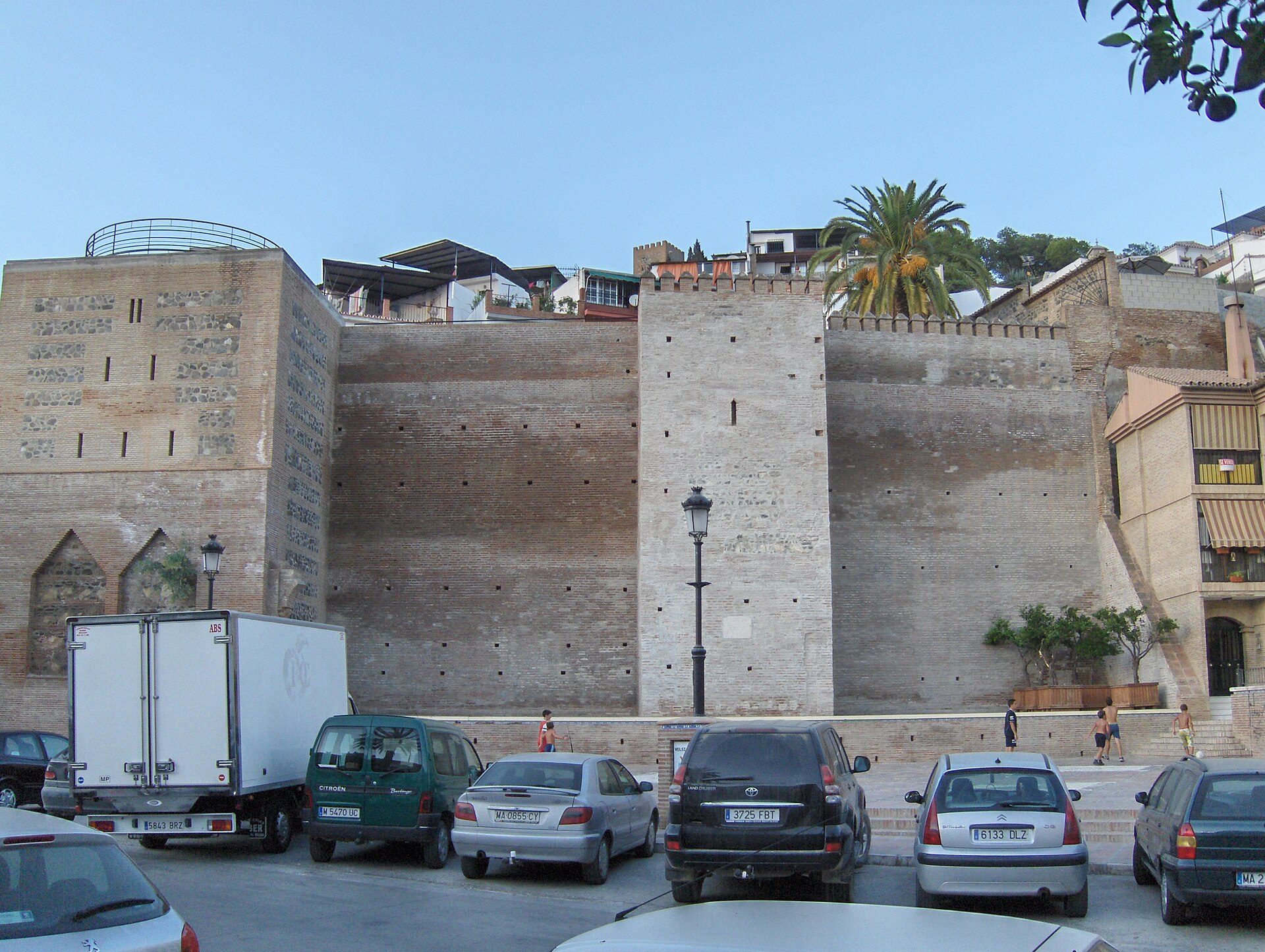 A historic stone building with a view of palm trees and a parking lot.