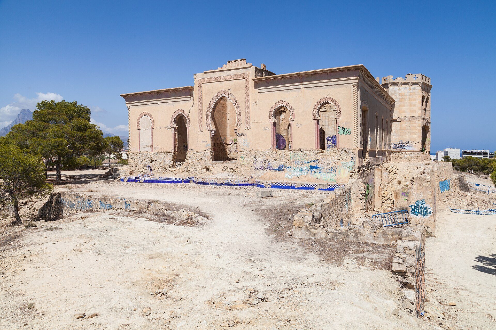 Old, dilapidated building with arched windows, surrounded by trees and mountains.