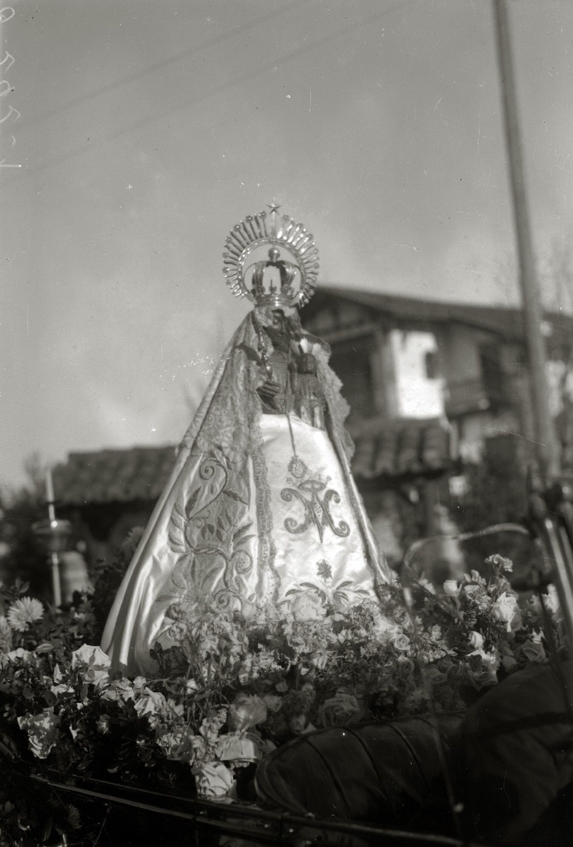 Alt text: Black and white photo of a religious statue adorned with flowers, set against a rural backdrop.