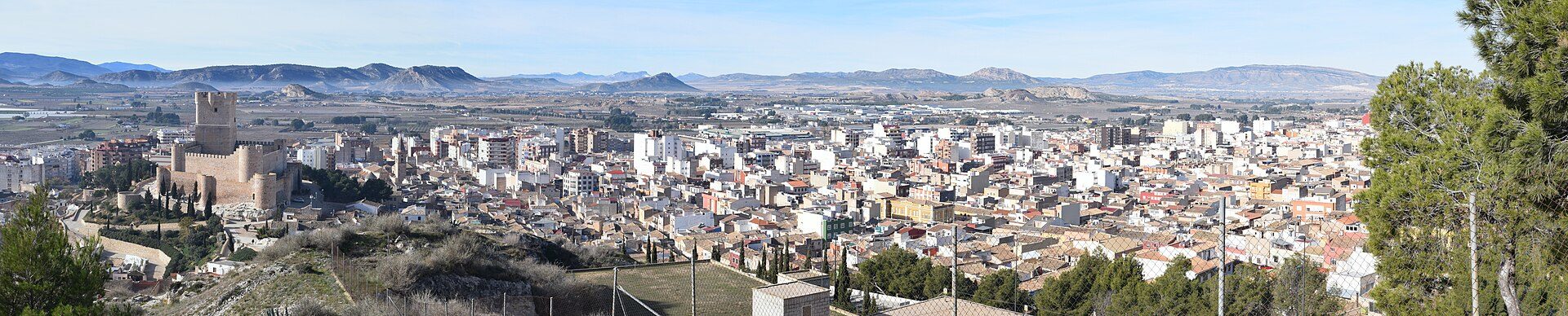 Aerial view of a city with a historic tower, surrounded by mountains and greenery.
