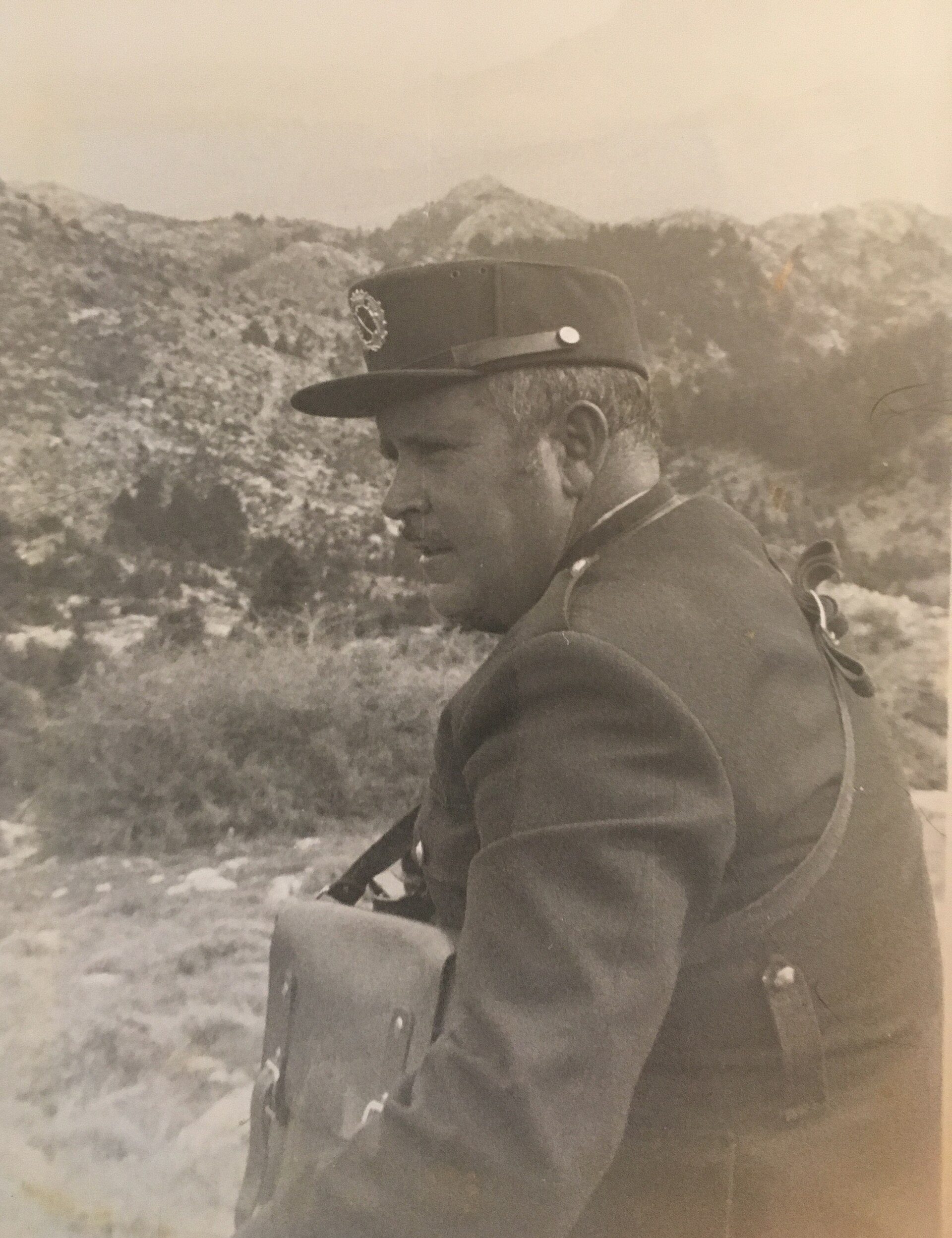 A vintage black-and-white photo of a man in a military uniform standing outdoors.