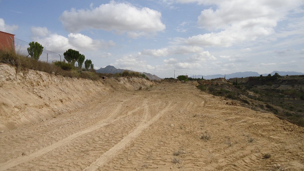An undeveloped plot of land with tire tracks in the dirt, overlooking a hilly landscape with mountains in the distance.