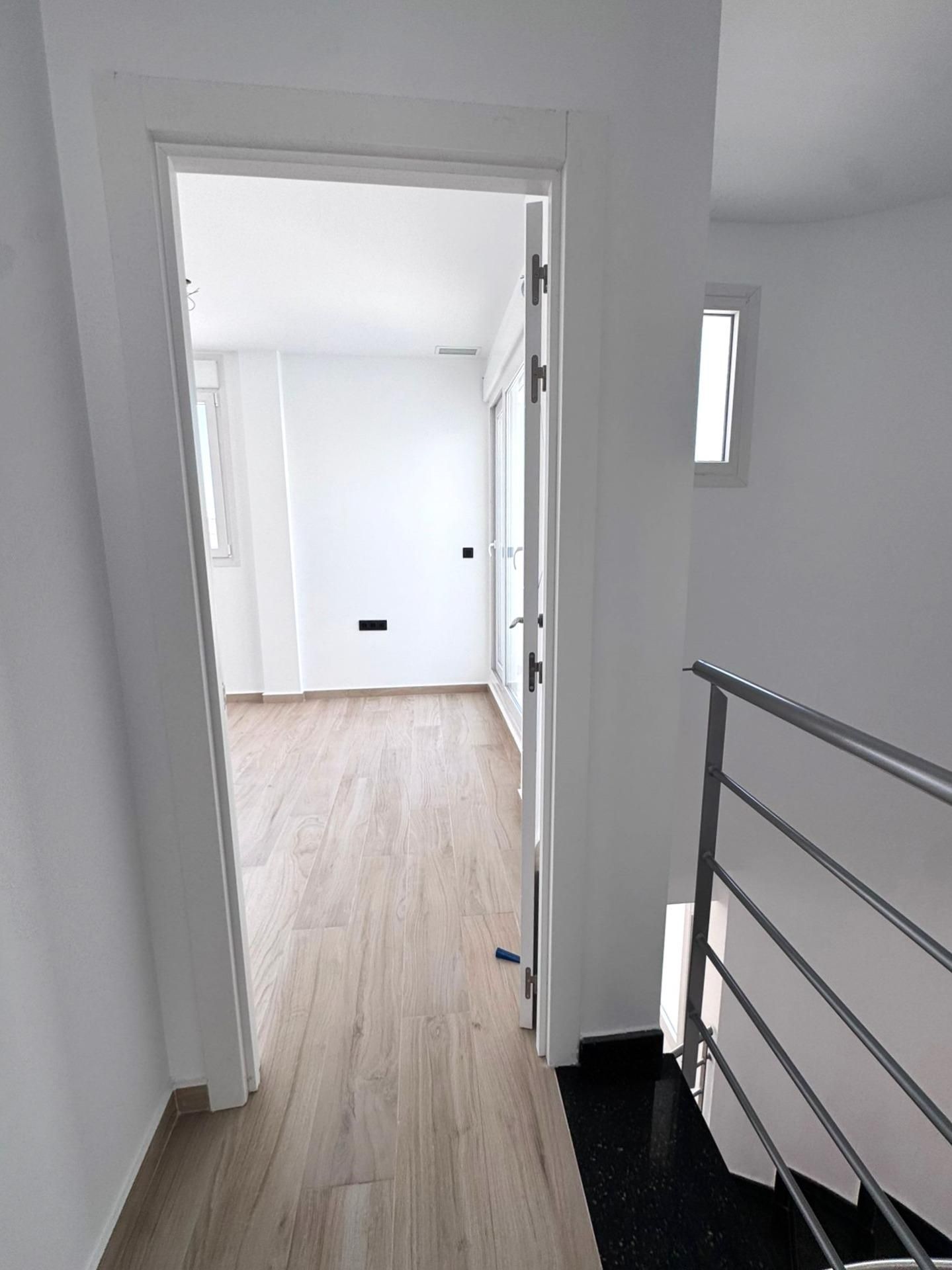 Modern wit interieur met openstaande deur naar kamer met houten vloer.