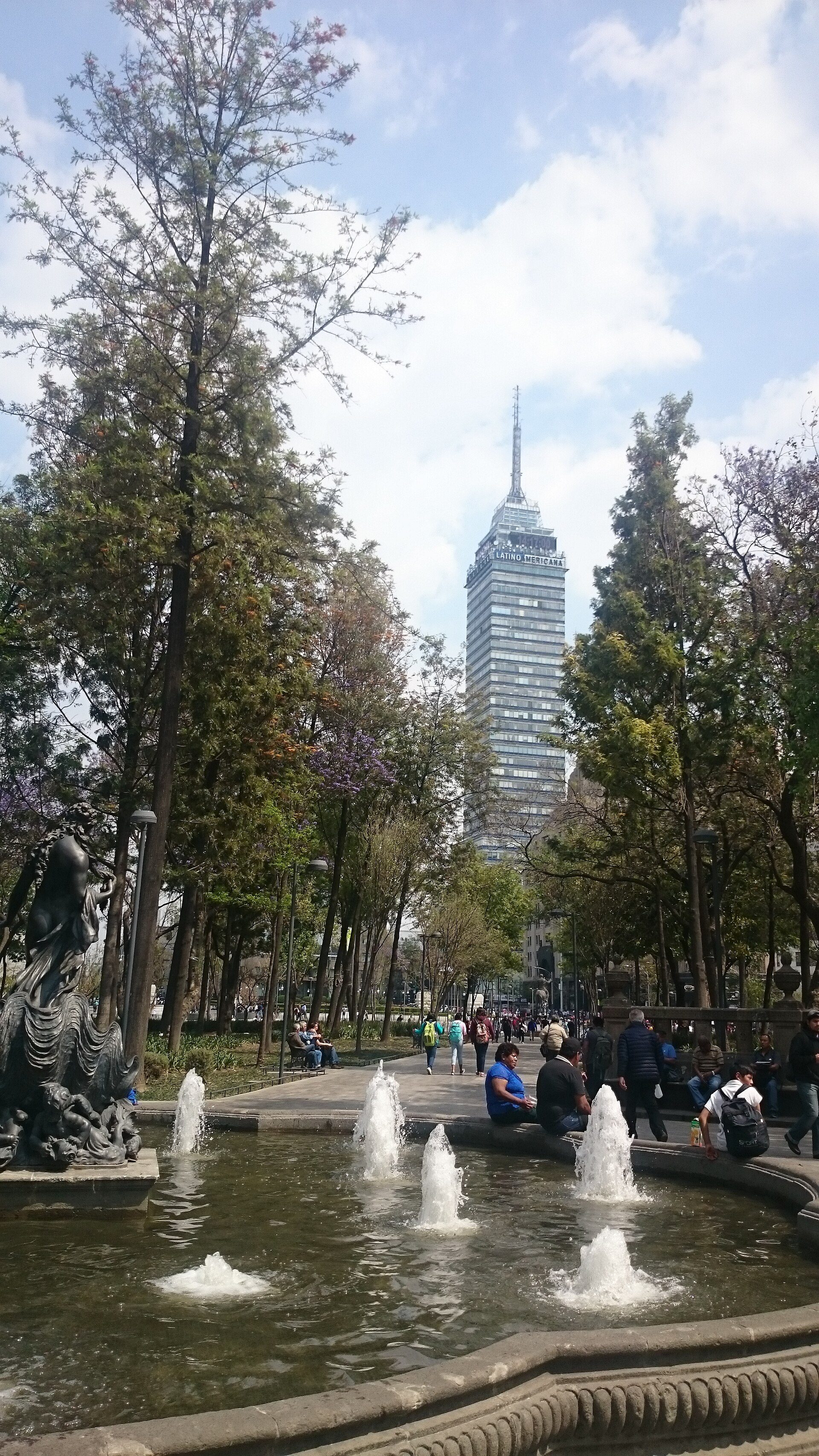 Alt text: Cityscape view from a modern room with fountain and greenery.