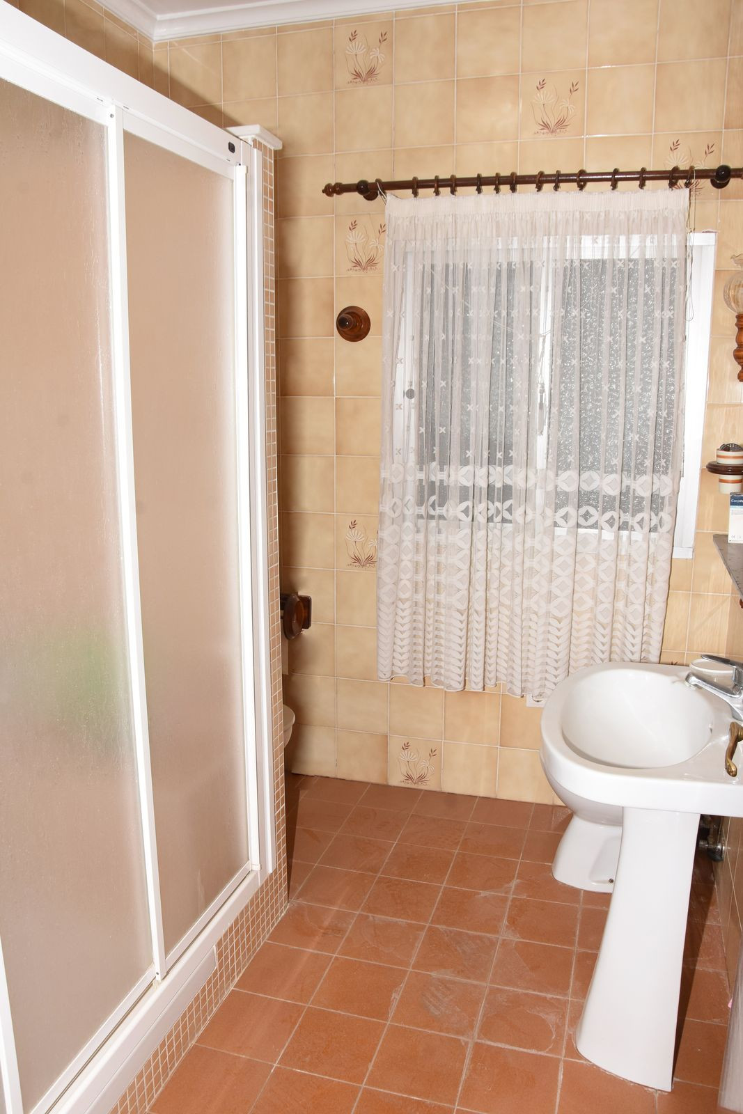 Badkamer met douchecabine, beige tegels en raam met gordijn.