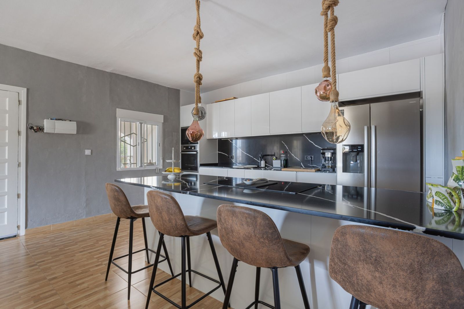 Moderne keuken met kookeiland, zwarte marmeren blad en bruine barstoelen.