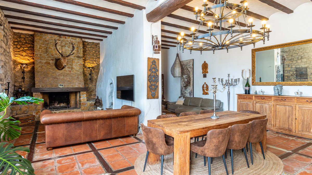 Spacious living and dining area with a stone fireplace, leather sofas, wooden dining table, and ornate chandelier.