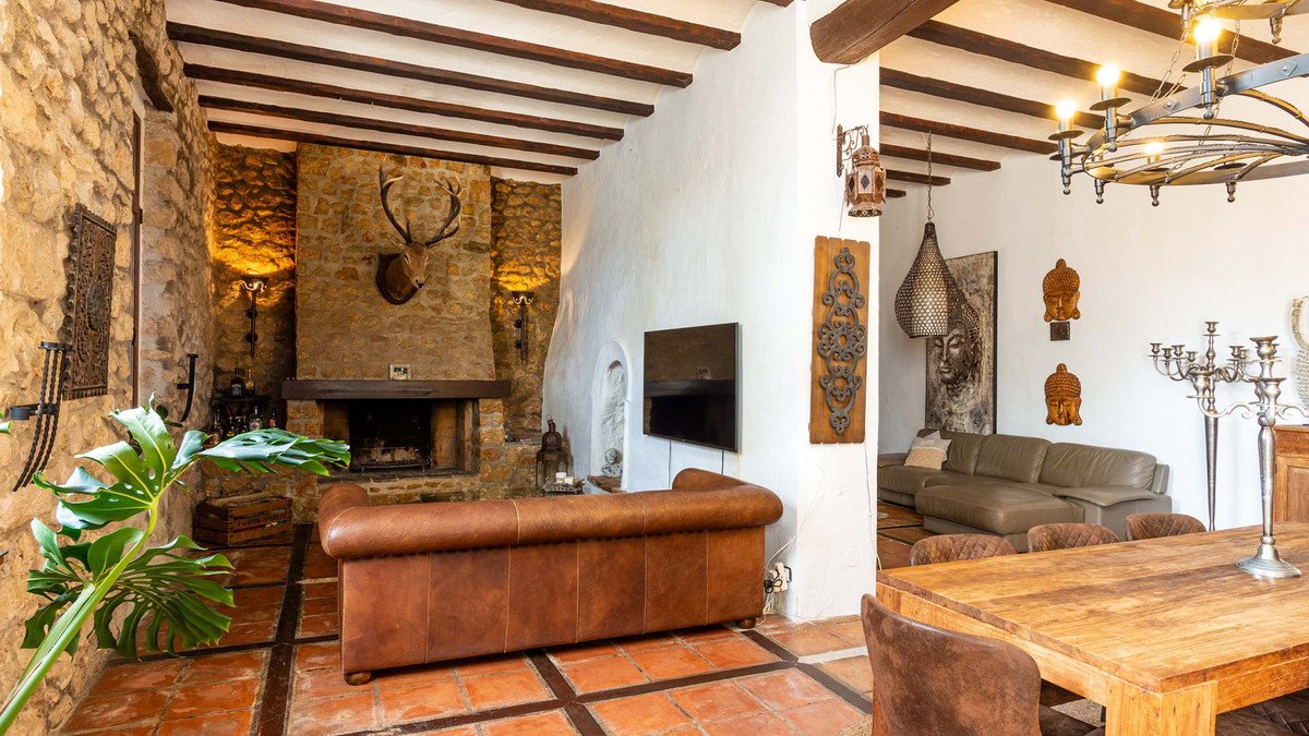 Spacious living and dining area with a large fireplace, leather sofa, TV, wooden beams, and terracotta floors.