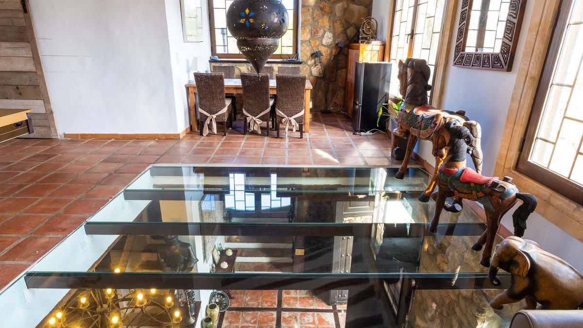 Dining area with rustic chairs and table, reflected in a glass floor with decorative elements visible below.