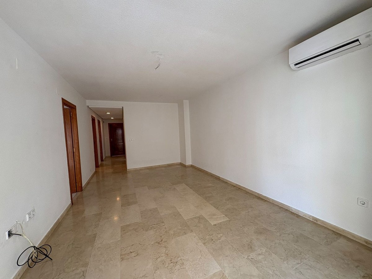 Spacious, empty living room with marble floors, white walls, an air conditioning unit, and several interior doors visible in the hallway.