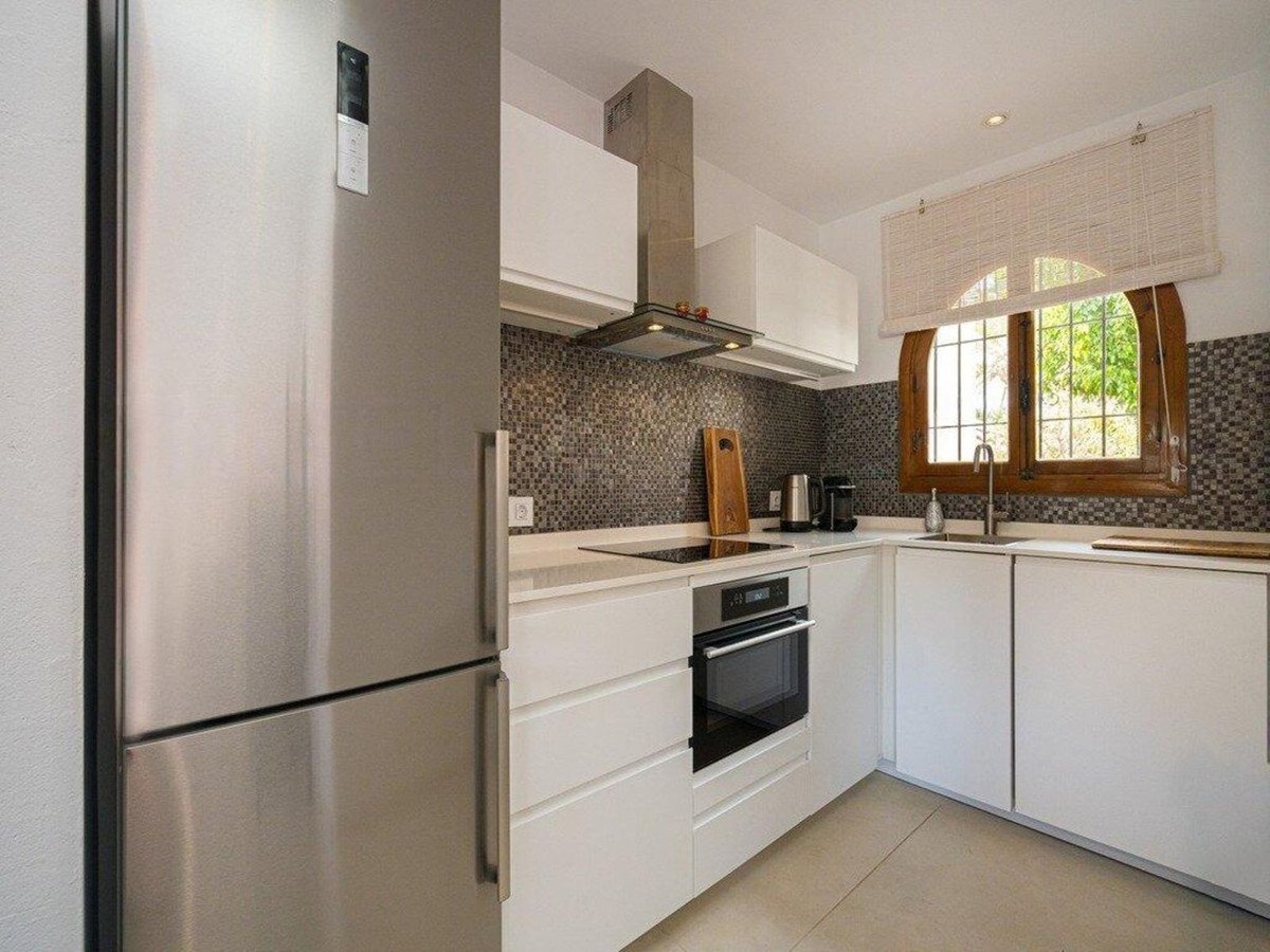 A modern kitchen with white cabinets, stainless steel refrigerator and oven, and a window with a view of greenery.