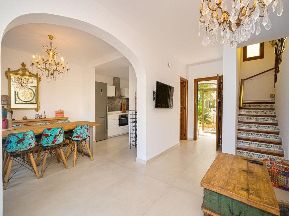 Dining area with patterned chairs, open archway to kitchen, and stairs leading to upper level. View of an outdoor garden through an open door.