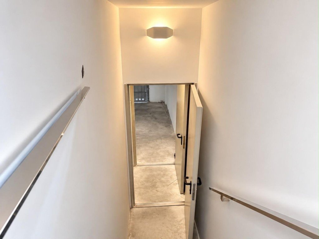 Stairwell with handrails leading to concrete-floored room, modern lighting