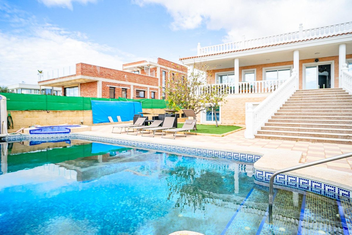 Swimming pool with lounge chairs and two-story house with stairs and balcony
