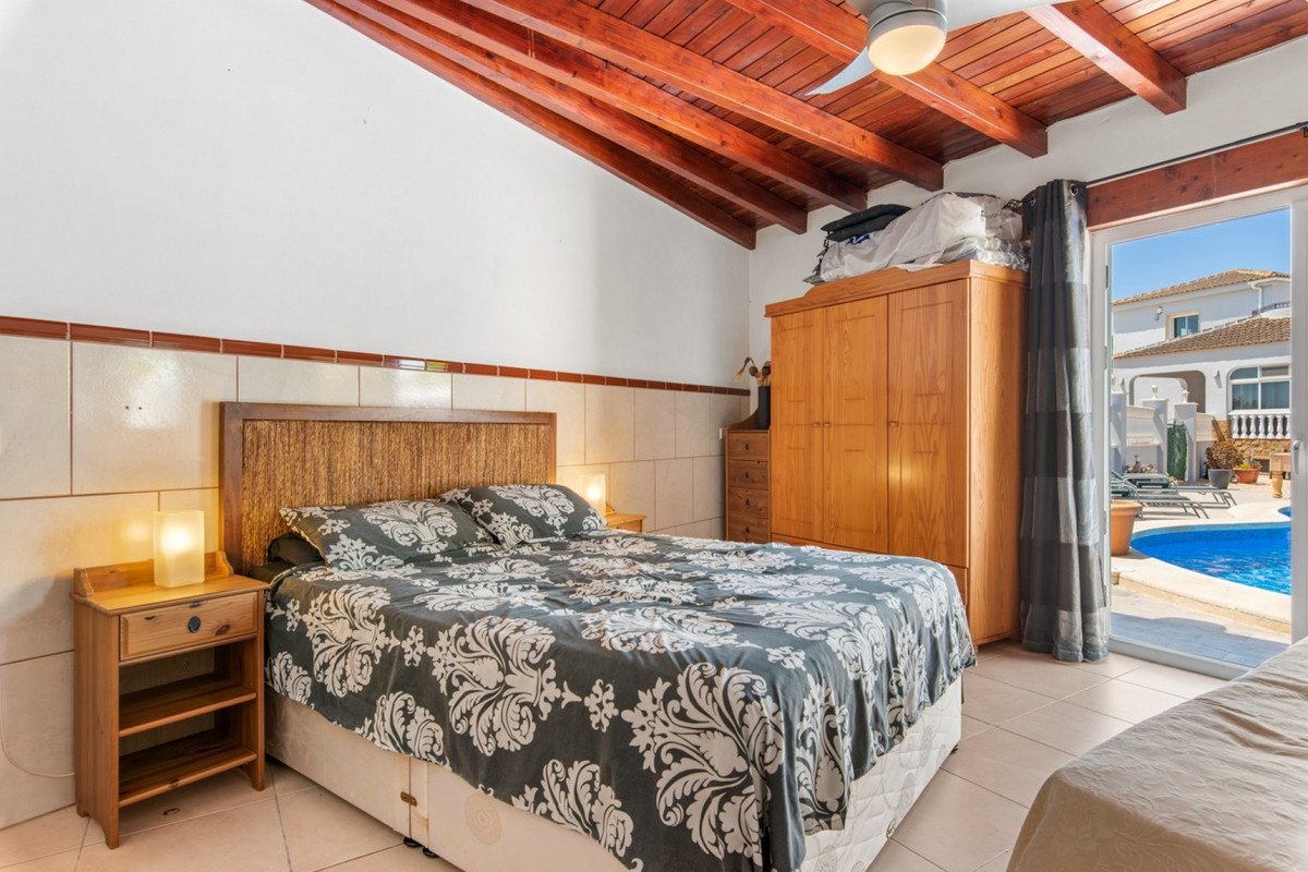 Bedroom with double bed, wooden wardrobe, and doors opening to a private pool area with lounge chairs.