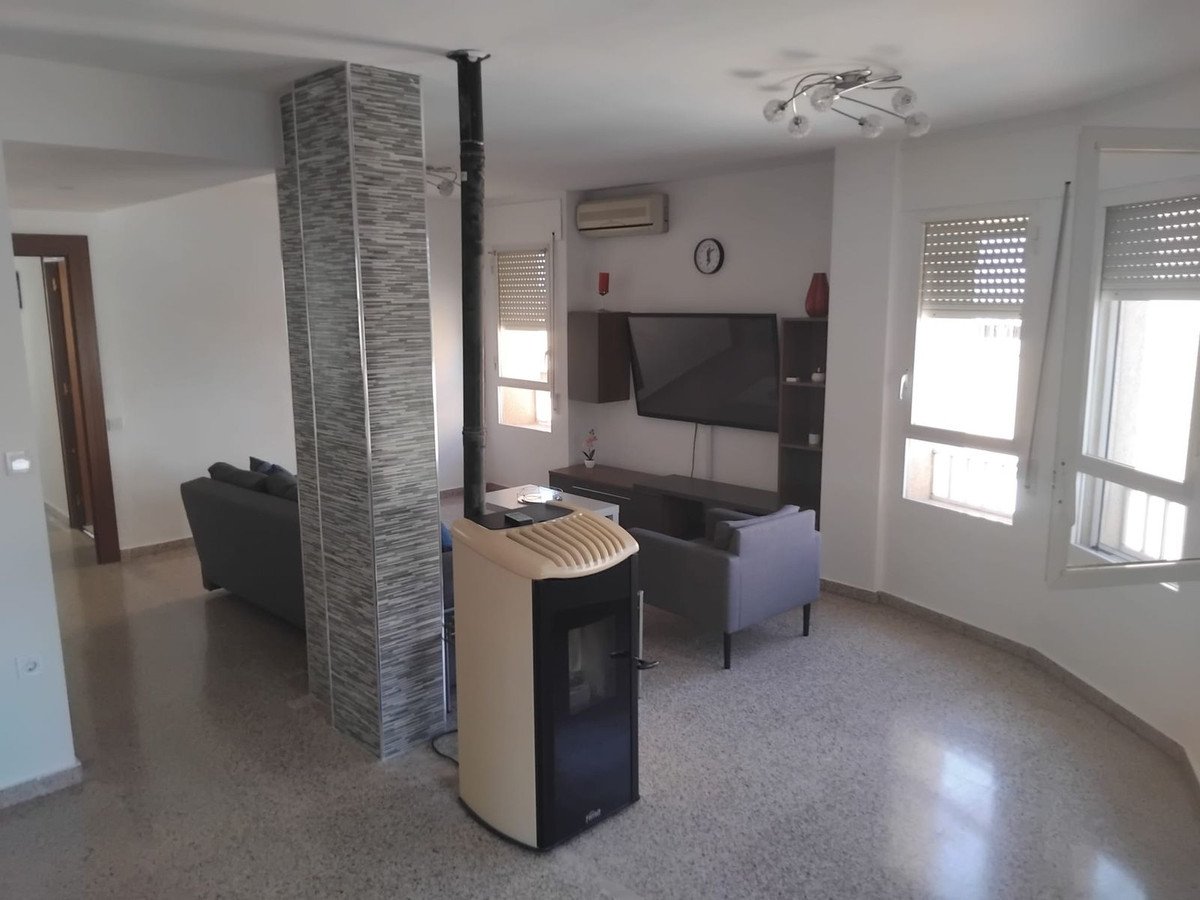 A living room with a pellet stove, sofa, television, and large windows with blinds letting in natural light.