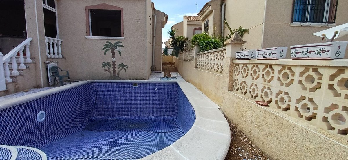 Empty tiled swimming pool with decorative palm tree mural on adjacent wall. Outdoor space with decorative planters.