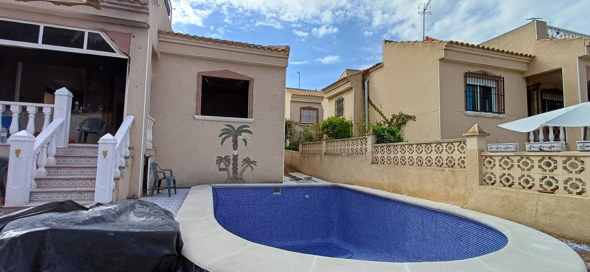 A bright outdoor space with a blue tiled swimming pool, decorative fence, and steps leading to the house entrance.