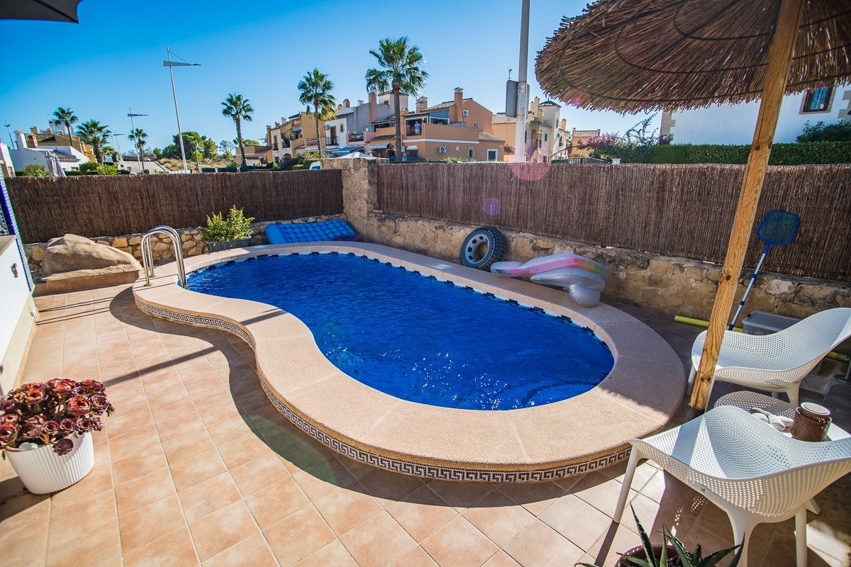 A private swimming pool with blue water, surrounded by a tiled patio, outdoor furniture, and a wooden-framed umbrella.