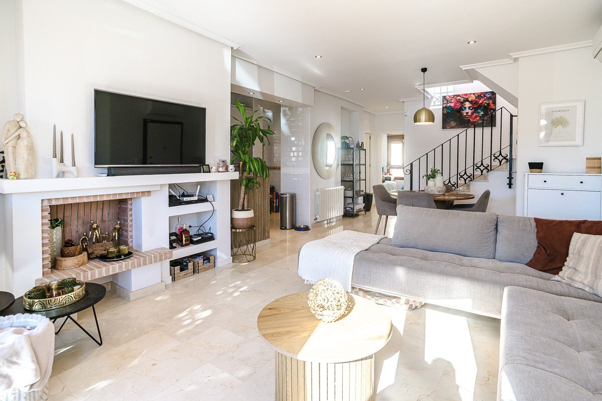 Spacious living room with a fireplace, TV, dining area, and staircase, furnished with a modern sofa and coffee tables.