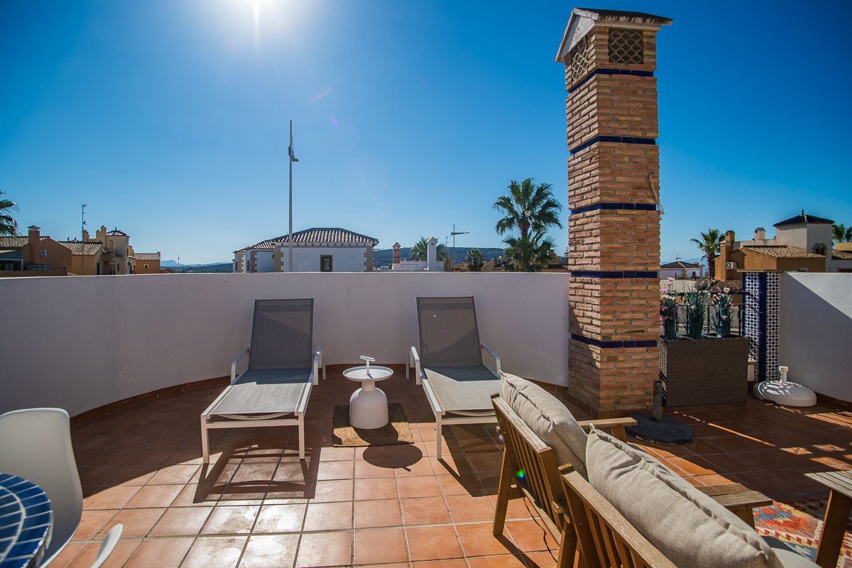 Terrace with lounge chairs, a brick chimney, and a view of rooftops under a bright blue sky.